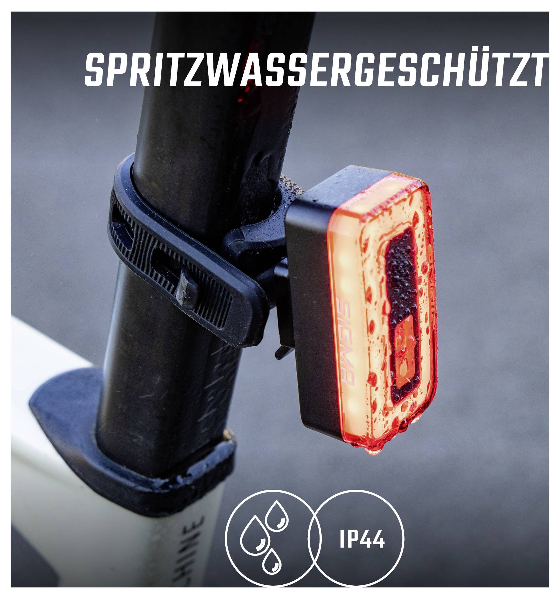 Close-up van een aan het frame gemonteerd rood fietserachterlicht met opdruk 'SPATWATERBESTENDIG' en aanduiding 'IP44'.
