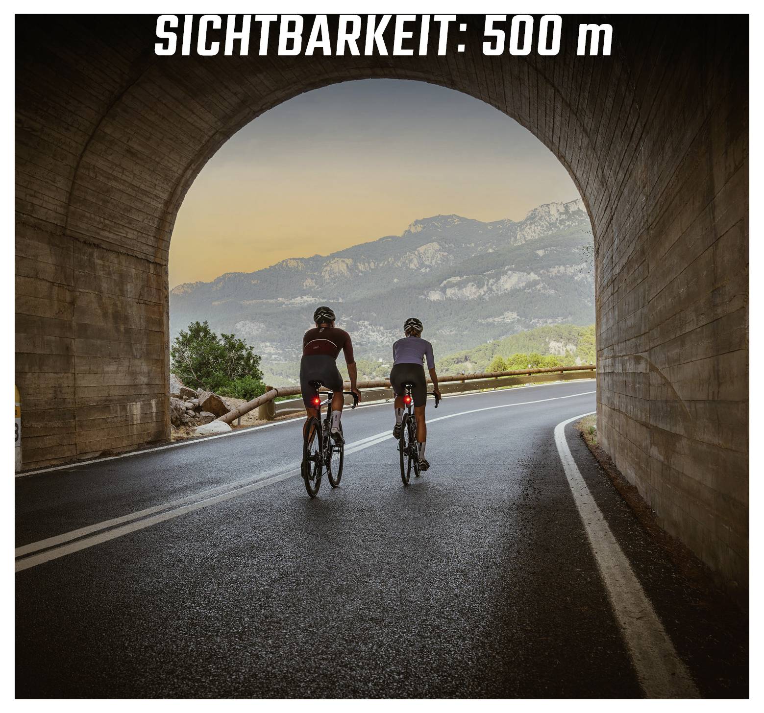 Twee fietsers rijden door een tunnel op een bochtige weg; bovenaan staat 'ZICHTBAARHEID: 500 m'.