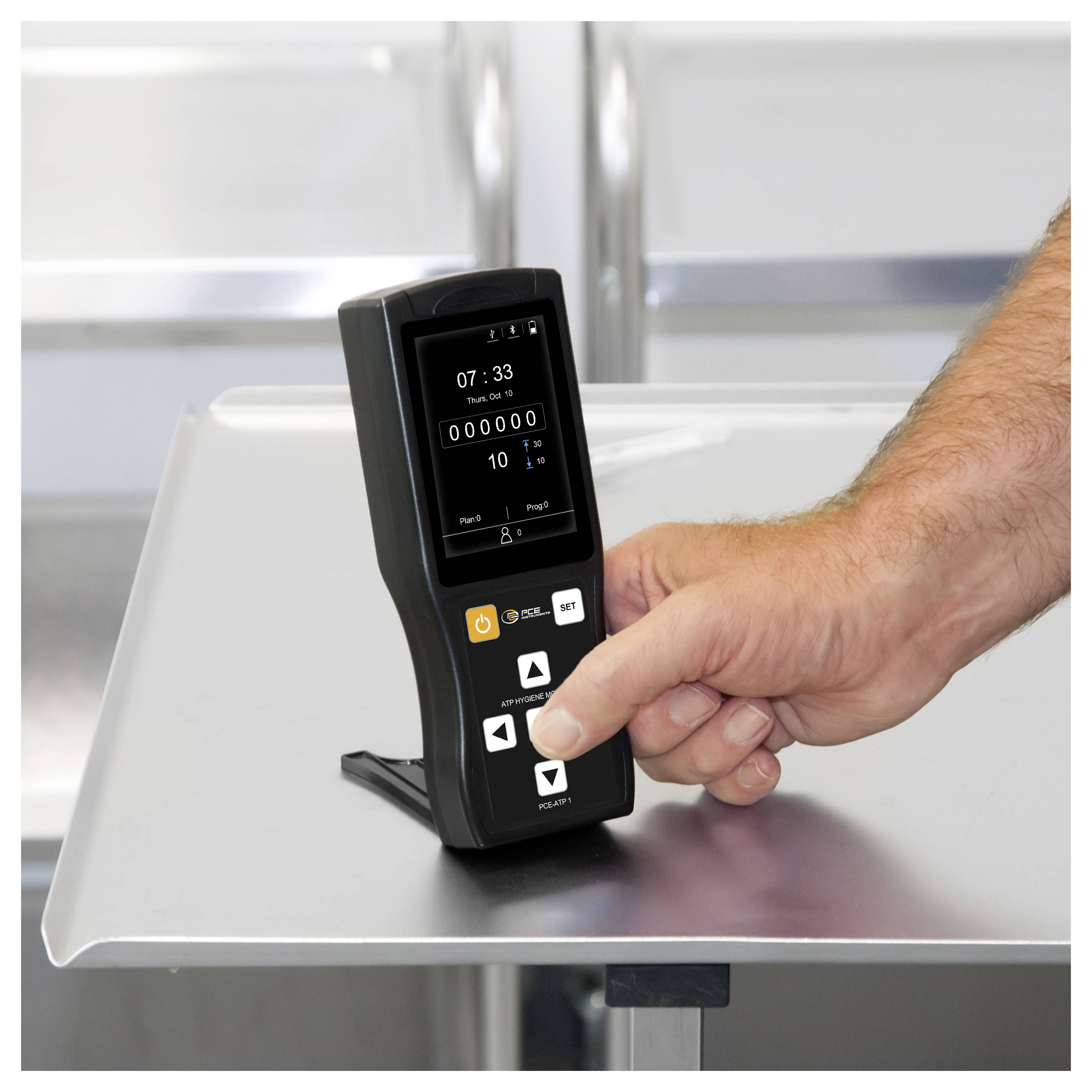 Hand drukt op knoppen van een zwart digitaal bedieningsapparaat met een klein scherm dat 07:33 en teller 000000 weergeeft op een metalen tafel.
