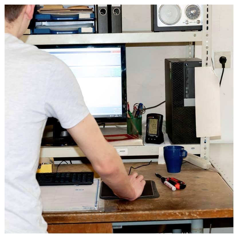 Persoon die aan een bureau werkt met behulp van een computer met een monitor, toetsenbord en muis in een klein kantoor of werkplaats.