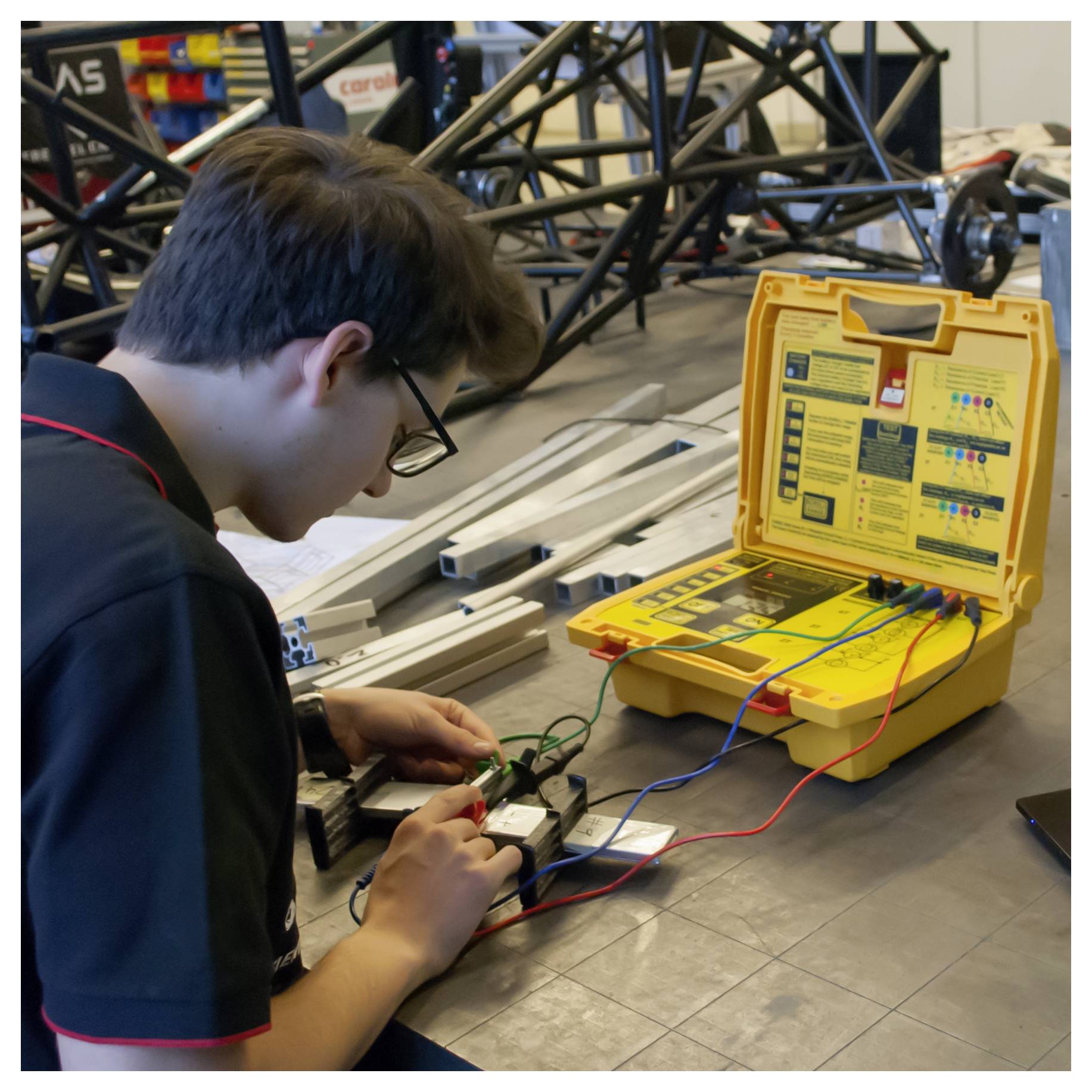 Technicus die elektronica test met een gele diagnostische koffer en kabels op een werkbank naast een chassisframe.