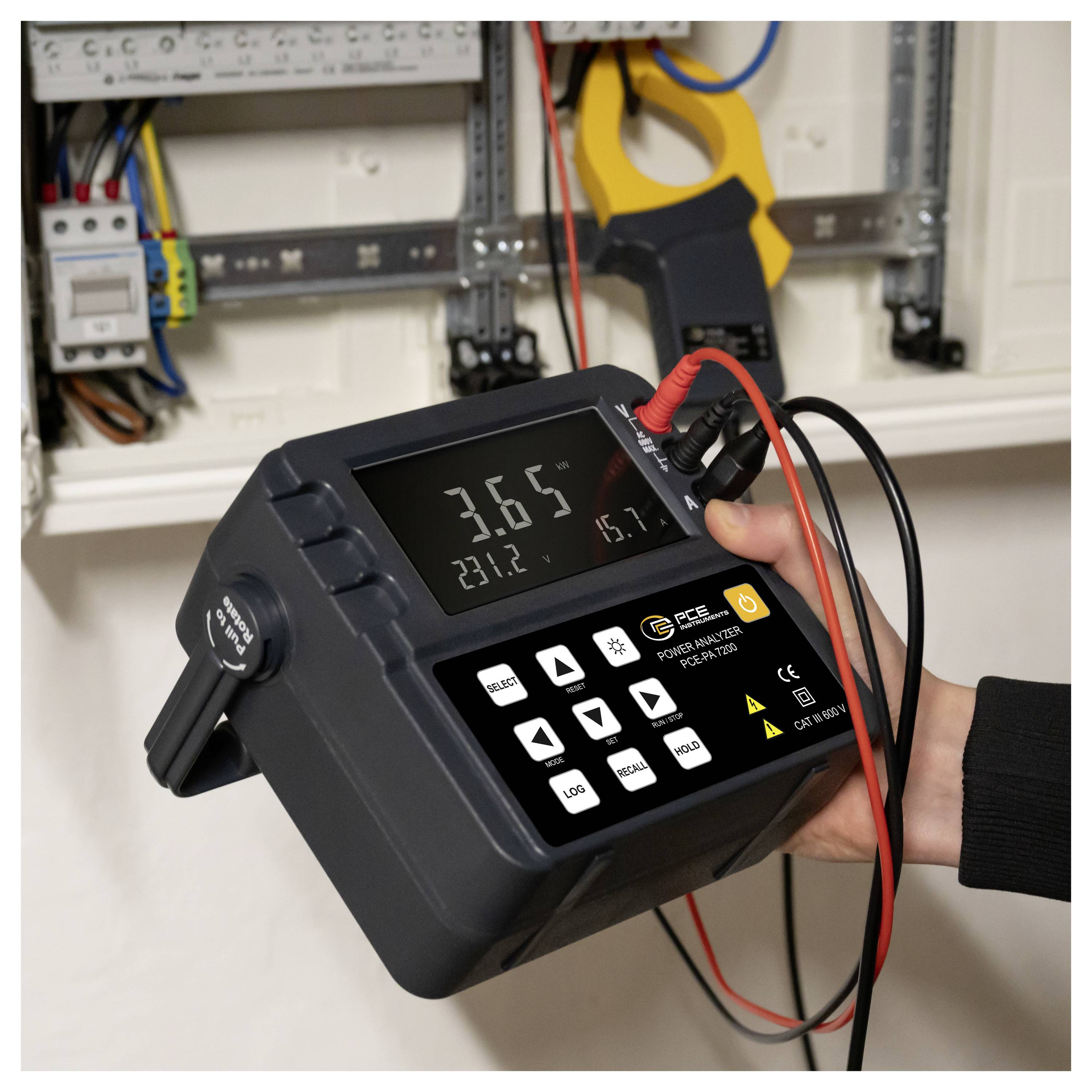 Handheld elektrische tester die metingen weergeeft bij een open circuitpaneel, met sondes verbonden met bedrading in een verdeeldoos.
