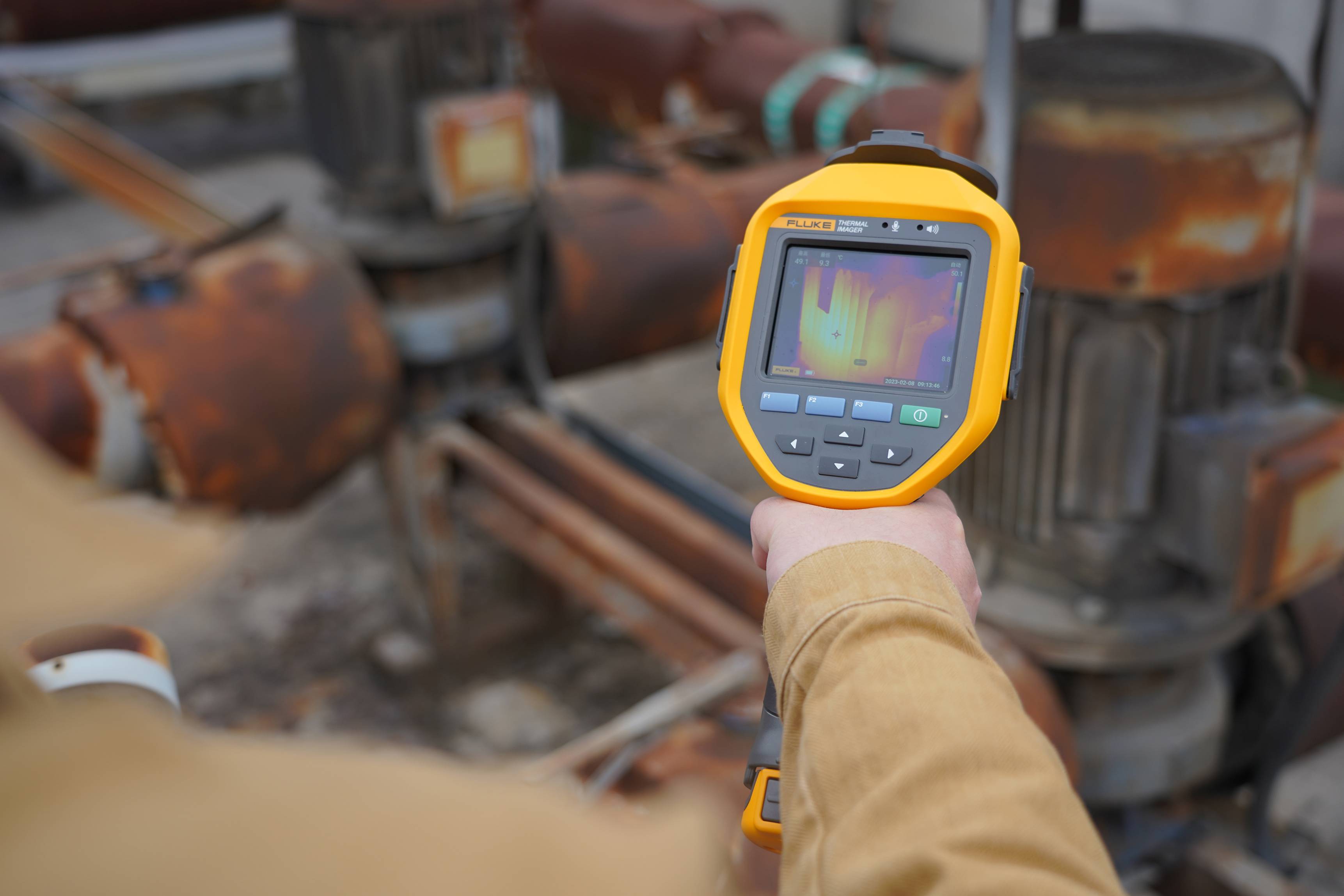 Een werknemer gebruikt een thermische camera om heet industrieel materiaal en buizen met zichtbare warmtepatronen te inspecteren.