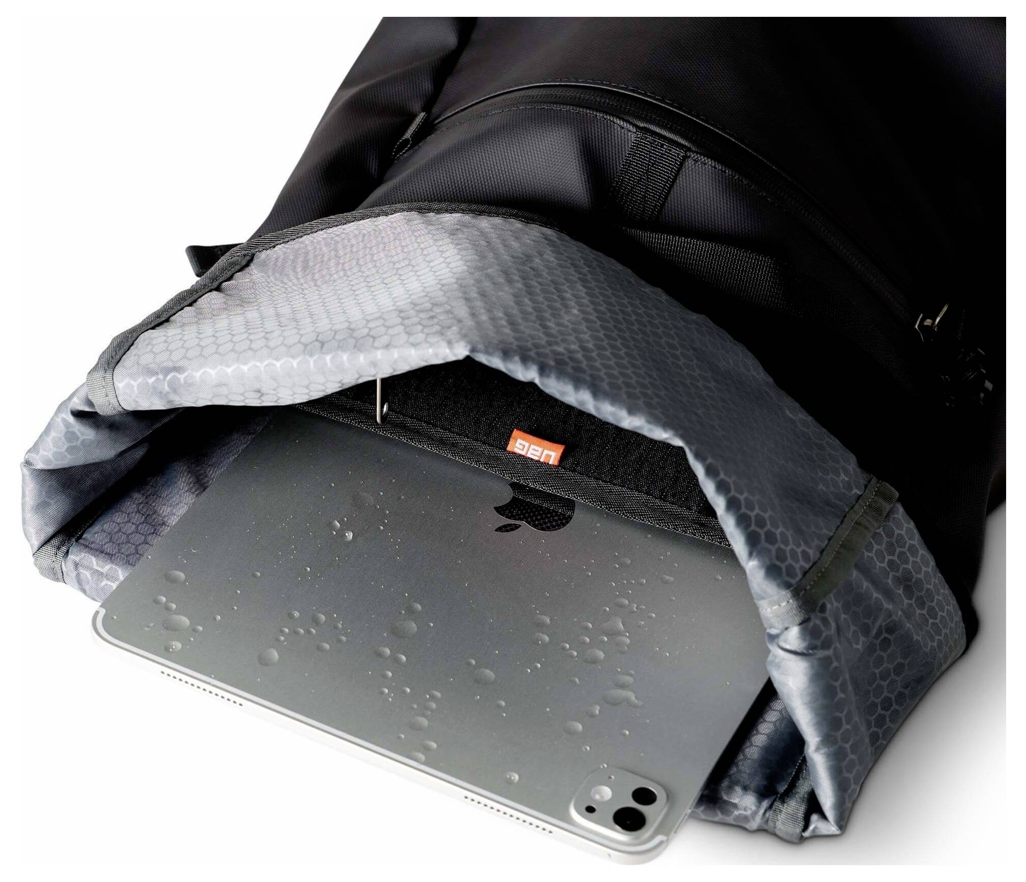 Tablet gedeeltelijk in een zwarte tas met een grijze gewatteerde flap, met waterdruppels op het oppervlak van de tablet.