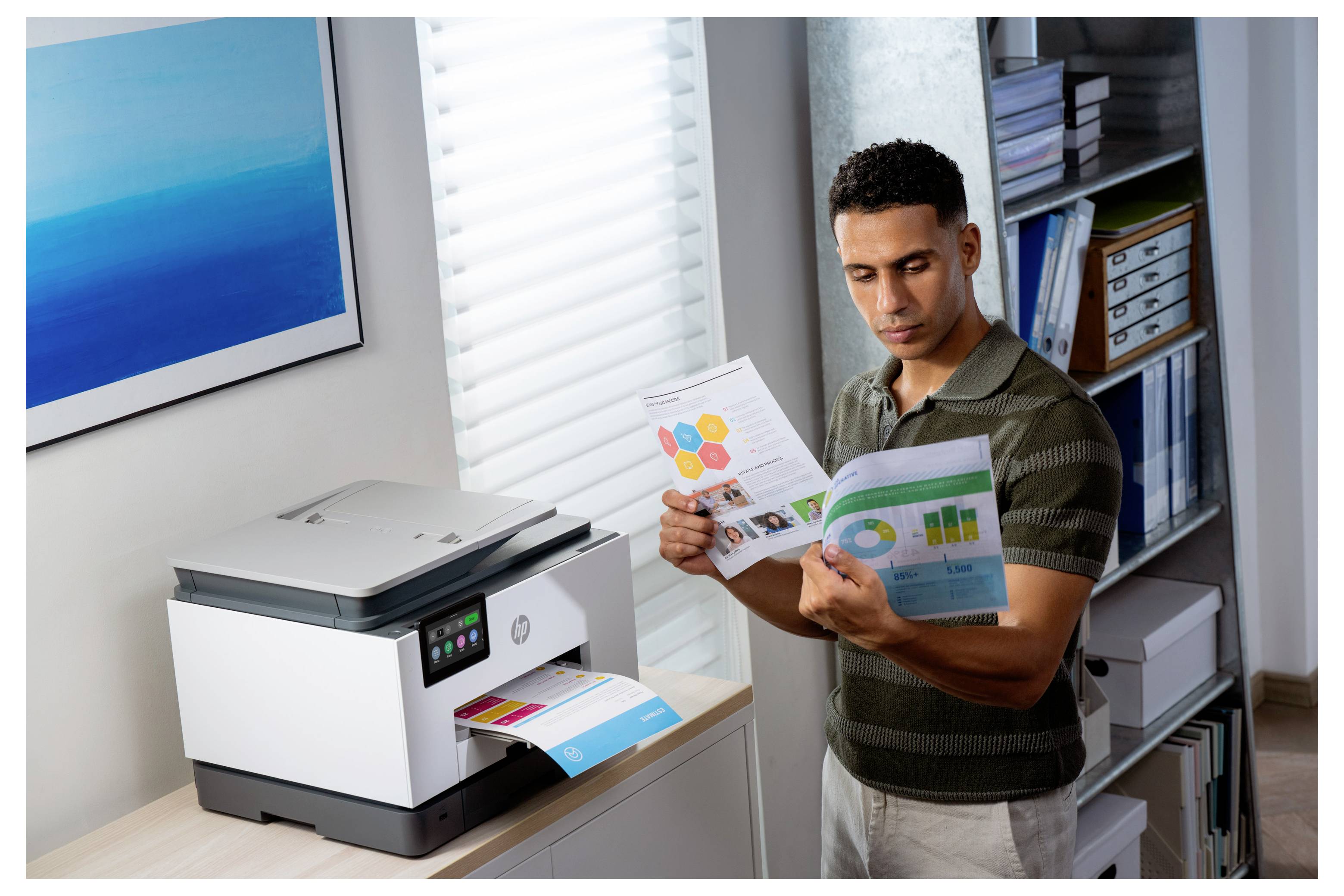 Man bekijkt afdrukken naast een HP-printer die een gekleurde pagina uitvoert in een kantoor.