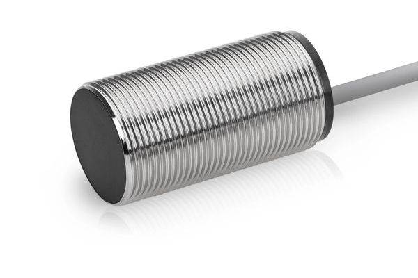 Een cilindrische metalen nabijheidssensor met een zilverkleurig schroefdraad lichaam en grijze kabel op een witte achtergrond.