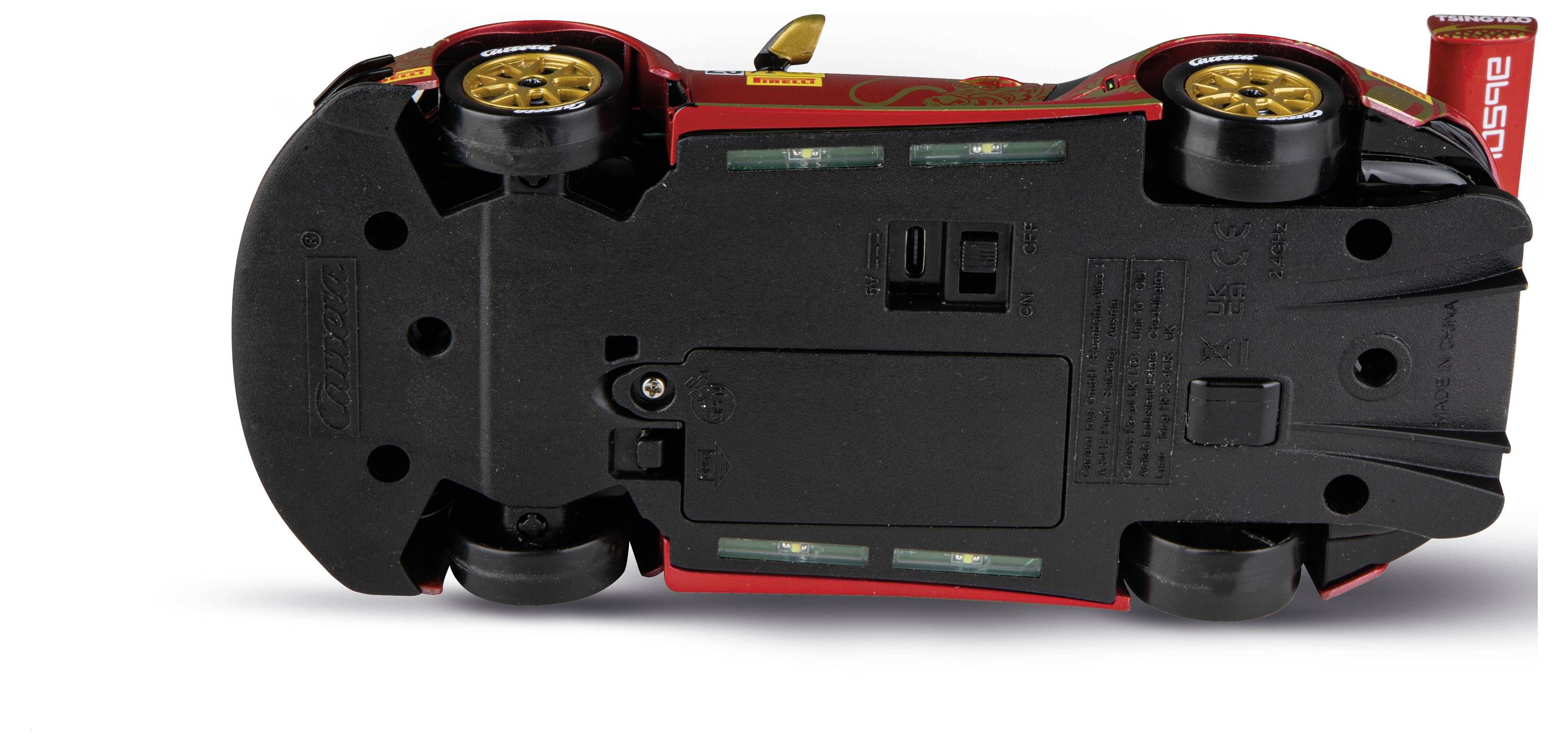 Onderkant van een rood-zwart speelgoedmodel van een sportauto, met wielen, batterijvak en schakelaar op een witte achtergrond.