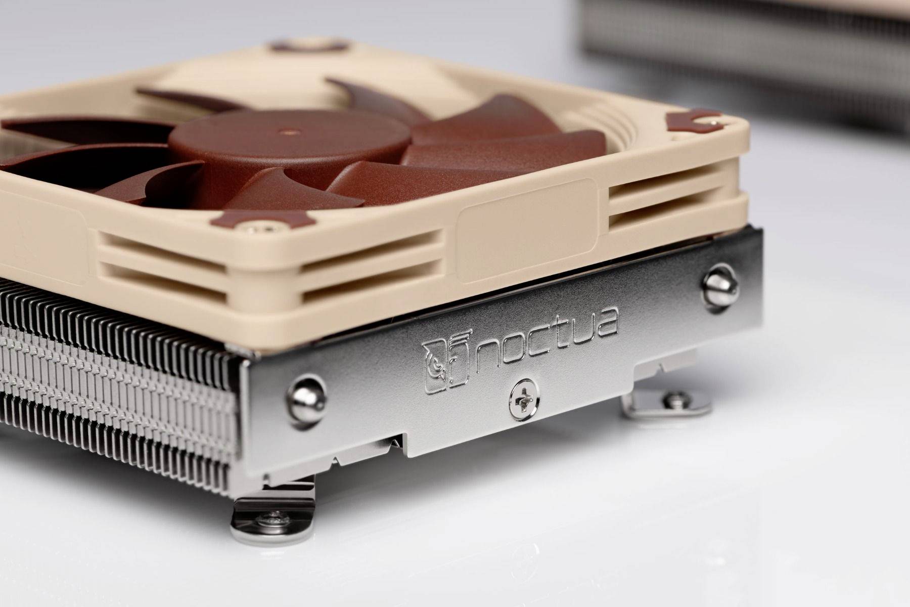 Close-up van een Noctua CPU-koelventilator en koellichaam met beige en bruine bladen op een wit oppervlak.