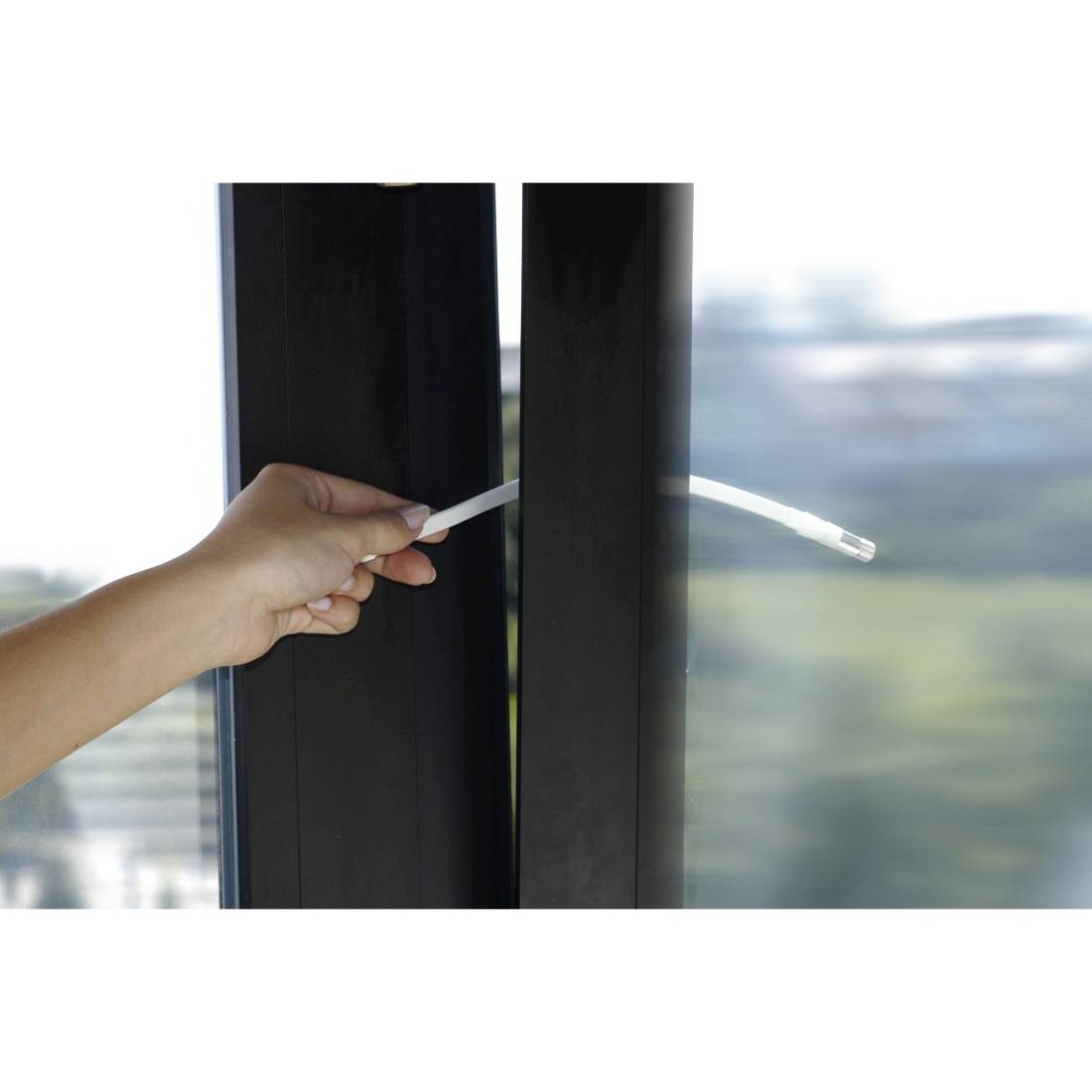 Hand die een raamkruk opentrekkt aan een raam met zwart frame en glas, met een wazig buitenuitzicht erachter.