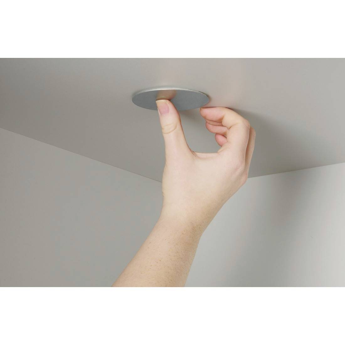Een hand drukt een ingebouwde plafondlamp of sensor in een plafondpaneel.