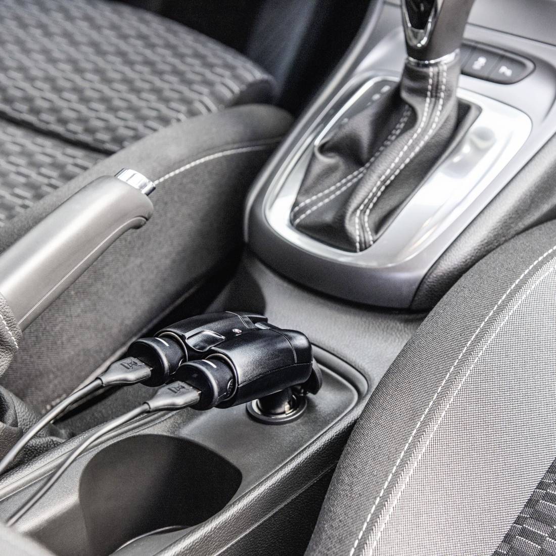 Middenconsole van auto met twee aangesloten oplaadkabels in een opslagvak naast de versnellingsbak.