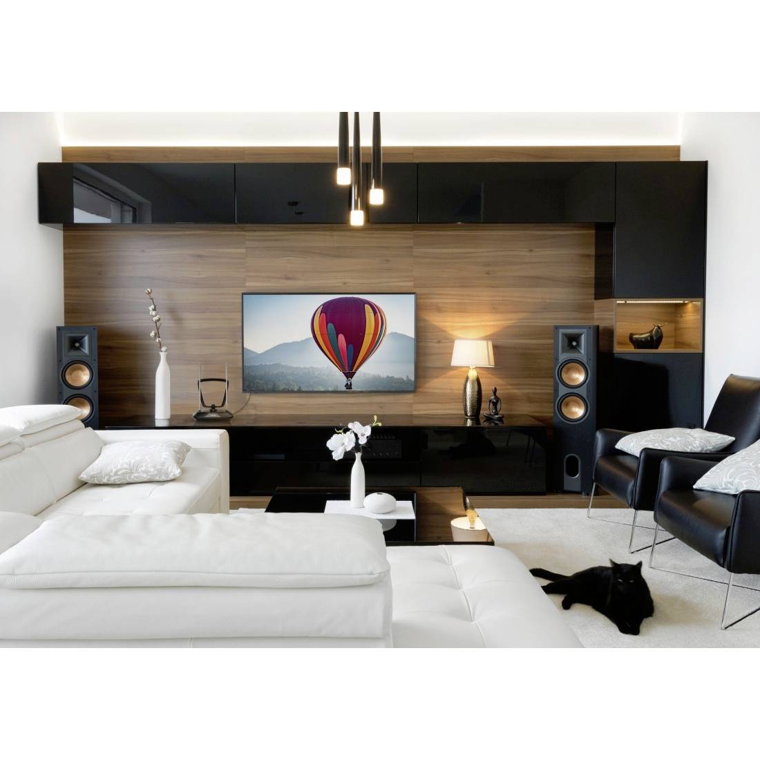 Moderne woonkamer met witte banken, zwarte stoelen, houten mediawand, luidsprekers en een tv met een luchtballon boven bergen.