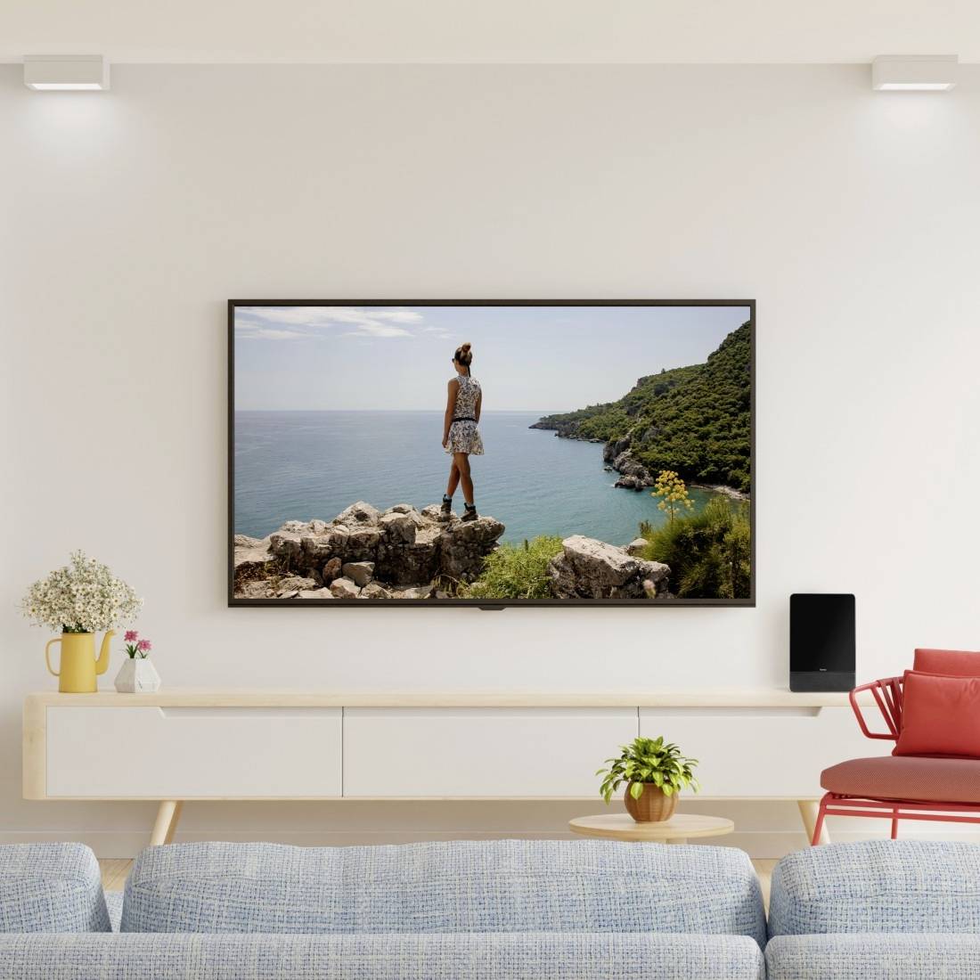Een aan de muur gemonteerde televisie toont een vrouw die op rotsen staat en uitkijkt over de zee en een groene kustlijn in een modern woonkamer.