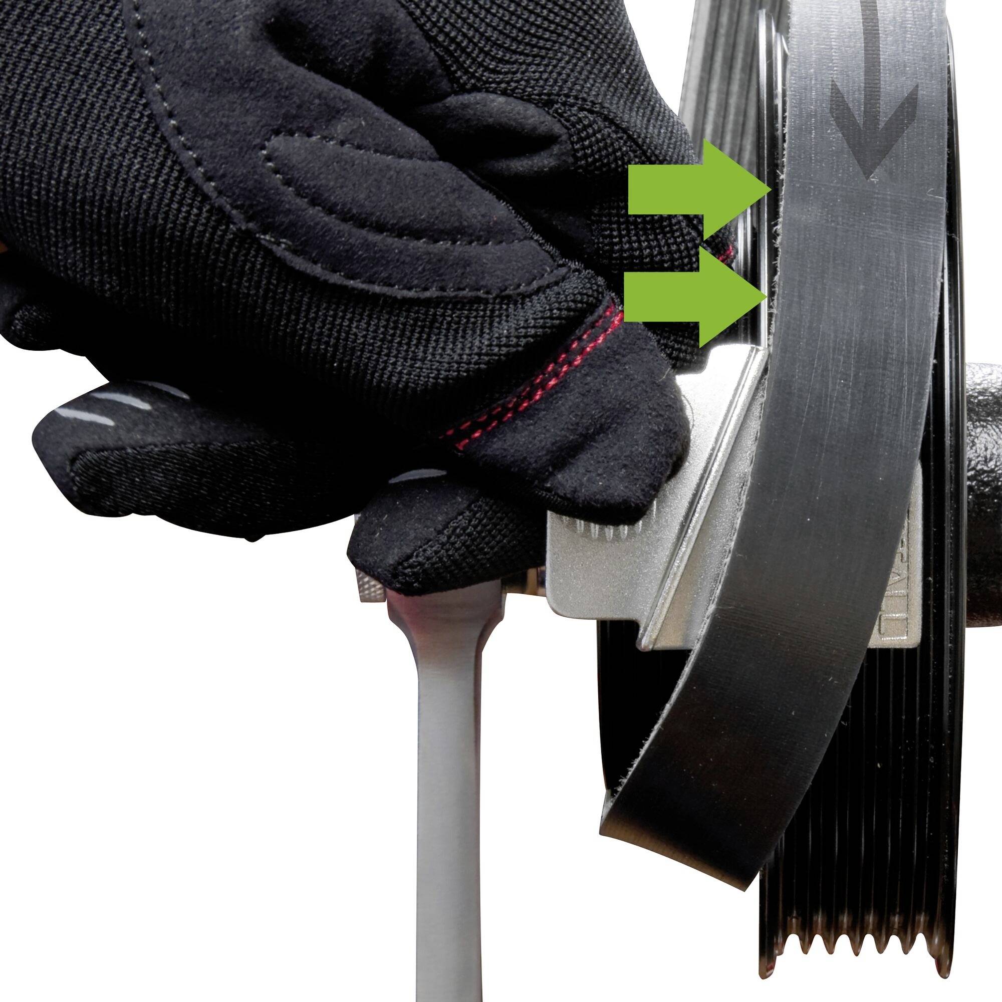 Gehandschoende hand drukt een grijs gereedschap tegen een zwarte riem met twee groene pijlen die uitlijning of drukpunt aangeven.