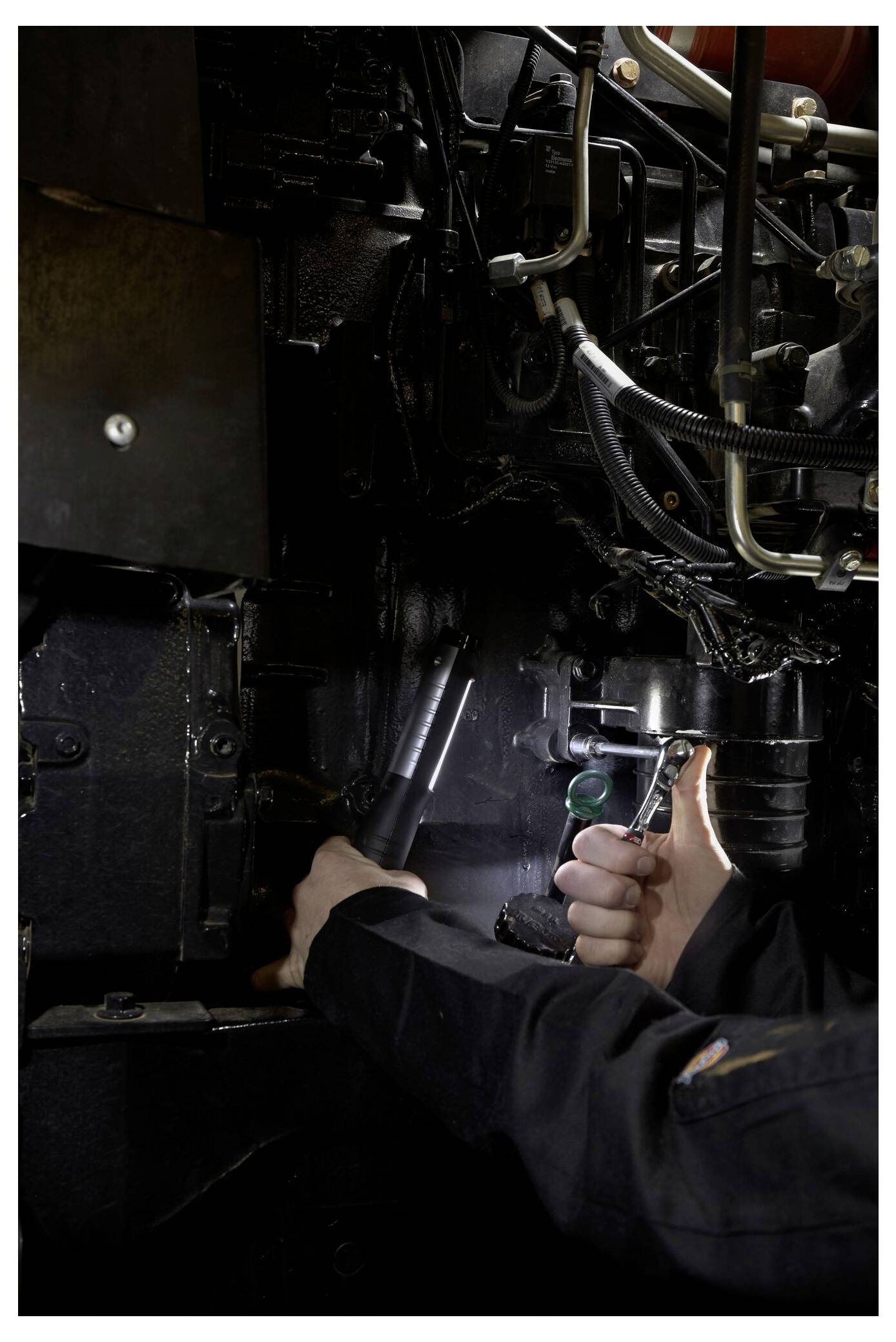 Technicus die een zaklamp gebruikt om machines in een donker industrieel motorcompartiment te inspecteren en repareren.