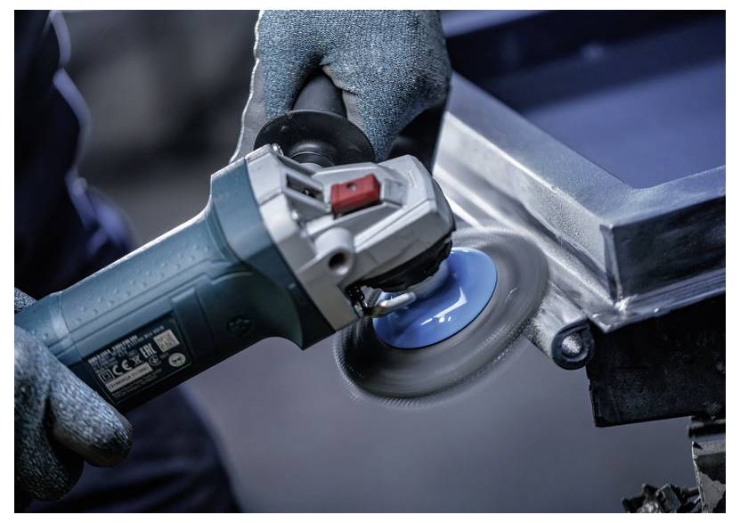 Gehandschoende handen gebruiken een haakse slijper om een metalen oppervlak te polijsten, waardoor een glad oppervlak op een glanzend industrieel onderdeel ontstaat.