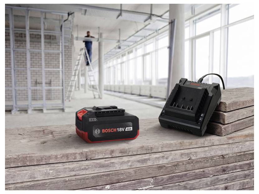 Bosch 18V batterij en lader op een houten werkbank in een helder, onafgewerkt vertrek, met een werker op een ladder op de achtergrond.