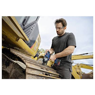 Man die een draadloze boormachine gebruikt op een spoor van een zwaar bouwmachine, draagt een veiligheidsbril op een buitenwerkplaats.