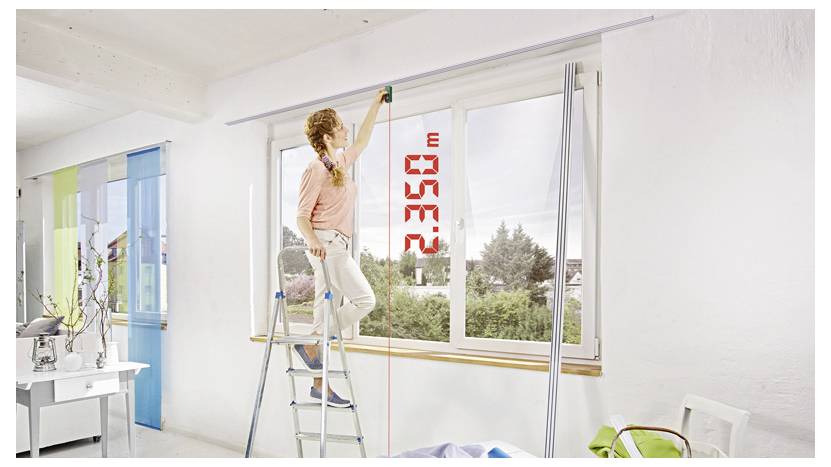 Vrouw op een ladder die de hoogte van een raam meet met een meetlint in een helder vertrek, met een rood digitaal display dat 2338 mm aangeeft.