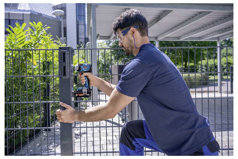 Man installeert een metalen hekpaal met een draadloze boormachine buiten in een zonnige tuin.