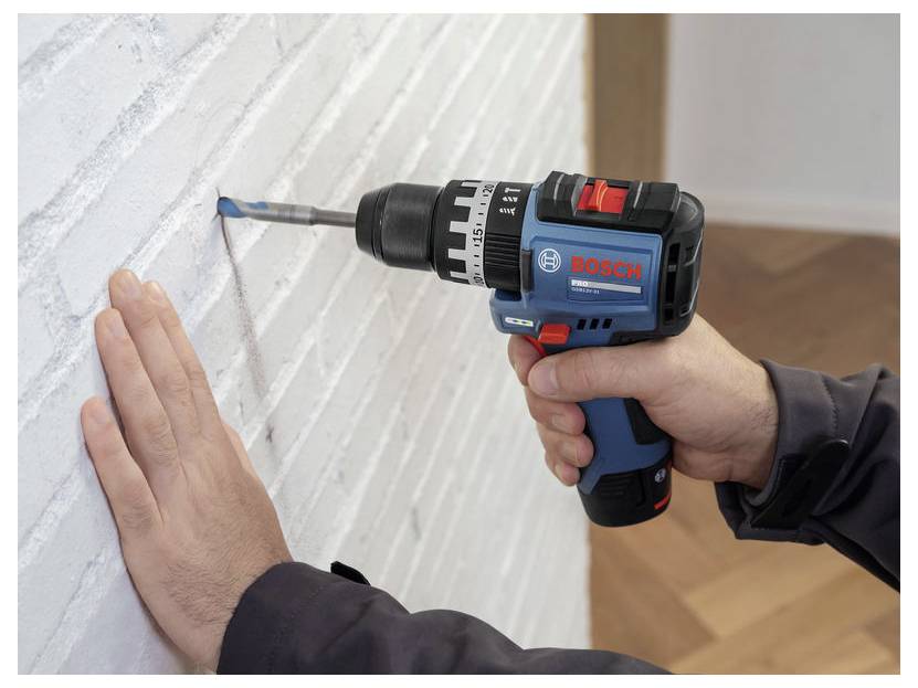 Persoon die een Bosch accuboormachine gebruikt om een bit in een witte bakstenen muur te boren terwijl hij het oppervlak met één hand stabiliseert.