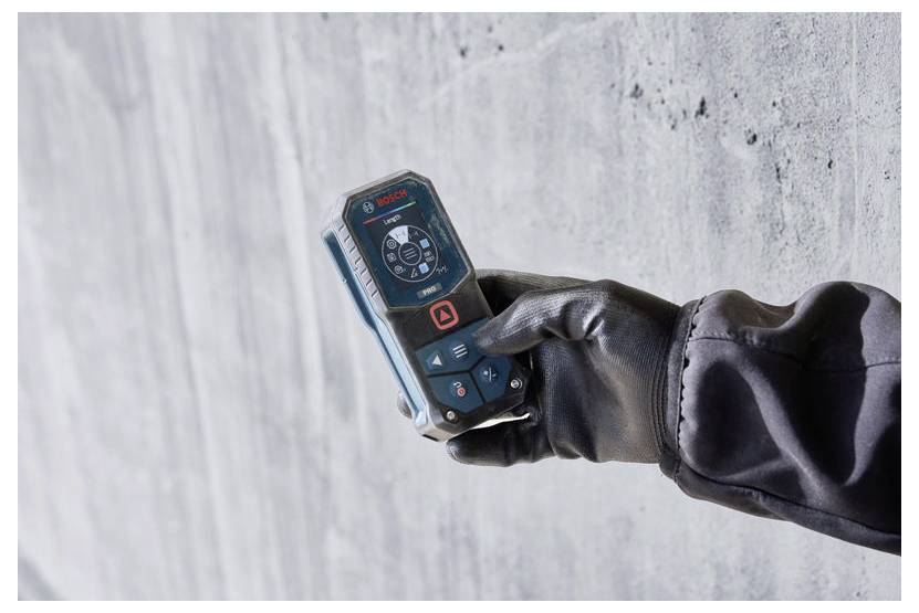 Gehandschoende hand die een Bosch-laserAfstandsmeter tegen een betonnen muur houdt, wat suggereert dat het gaat om nauwkeurig binnenmeten of bouwwerk.