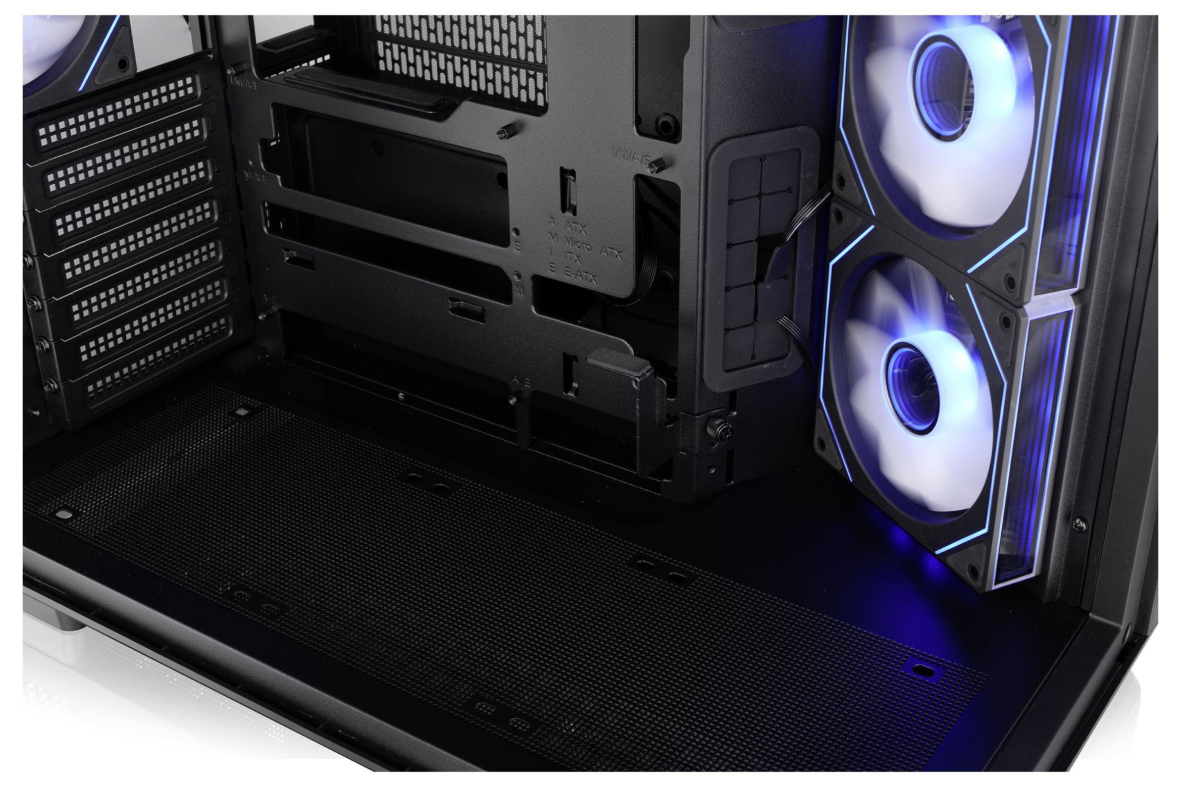 Binnenkant van een desktopcomputer-behuizing, waarin twee blauw verlichte koelventilators en een lege moederbordlade met kabelrouteringsruimte in close-up zijn afgebeeld.