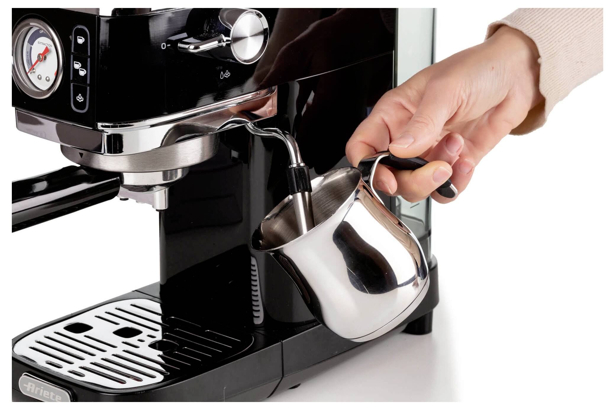 Hand die een metalen melkkannetje onder de stoommond van een espressomachine plaatst, in voorbereiding om melk op te stomen.