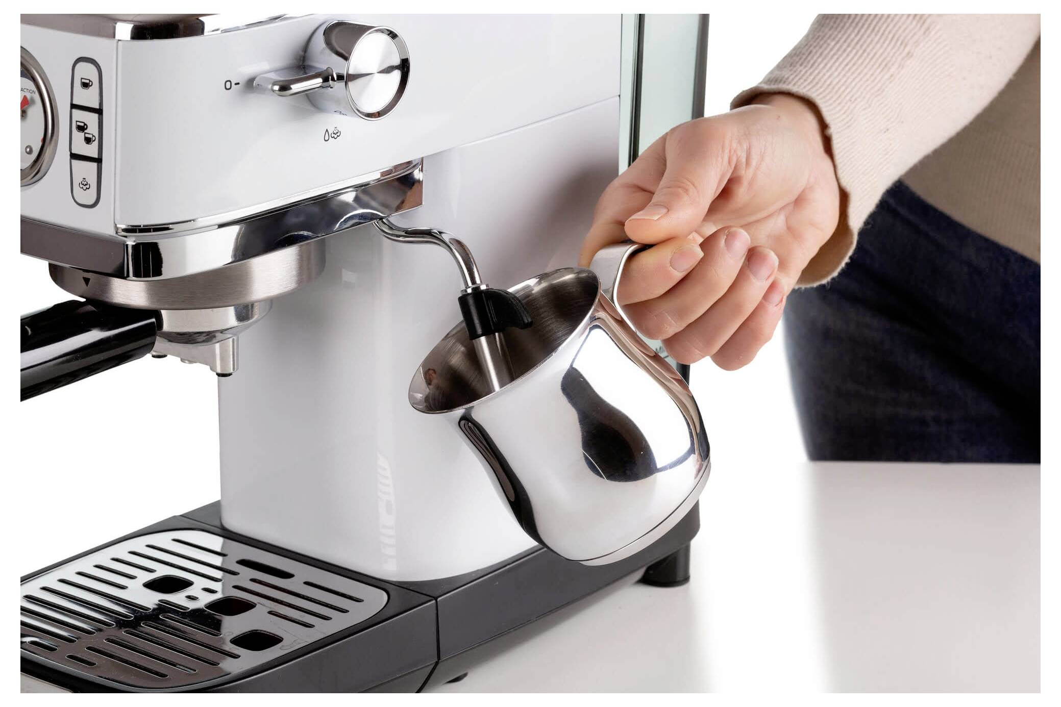 Hand die een roestvrijstalen koffiezetapparaat vult met een stoomende melkschuimkan onder de espressomachinesproeier.
