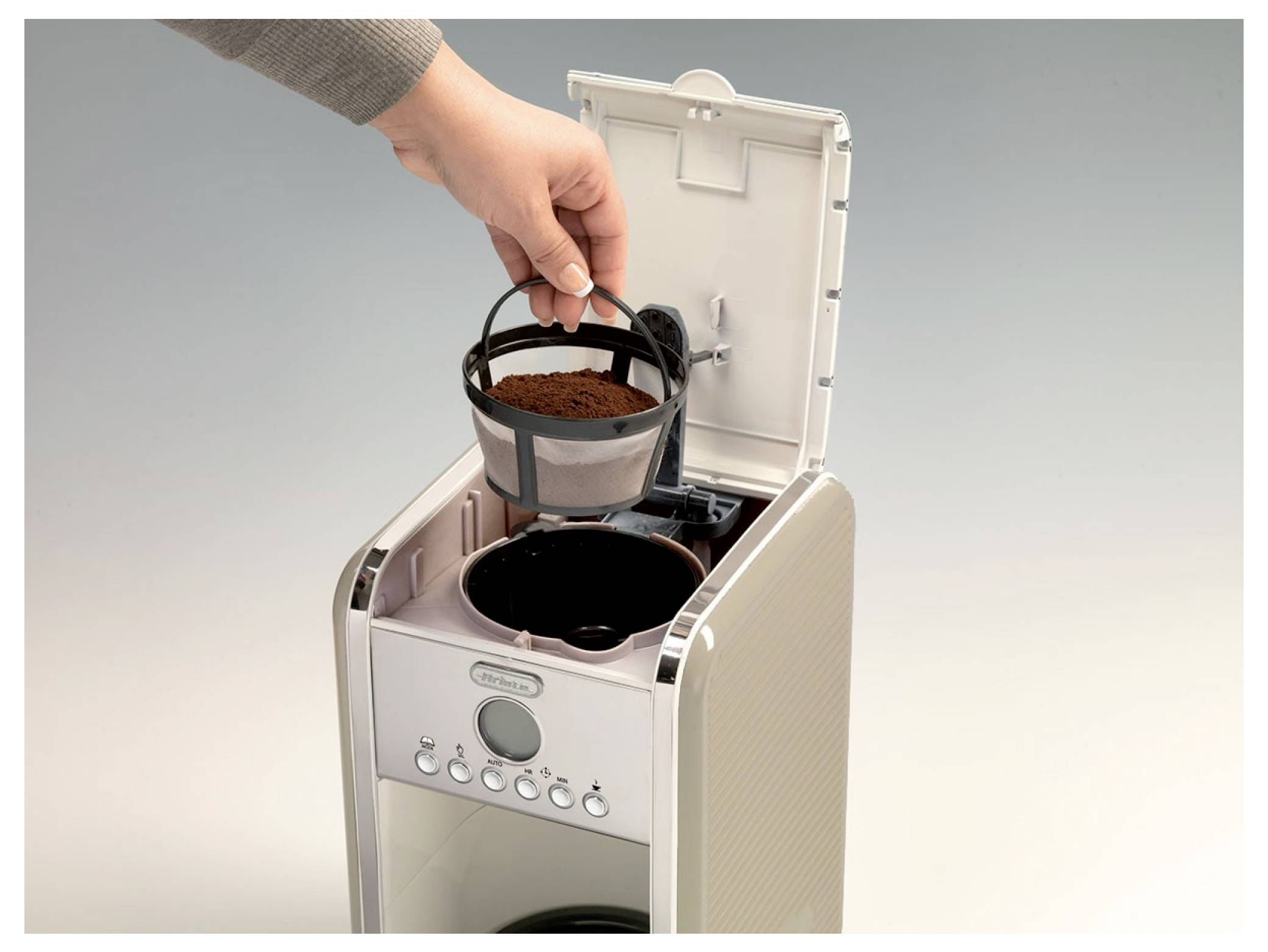 Hand die een koffiefilter met koffiedik in de open bovenkant van een koffiezetapparaat plaatst.