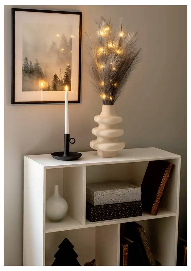 Wit wandrek met kaars, ingelijste wandkunst en gloeiende decoratieve takken in een vaas, wat een gezellige binnendisplay creëert.