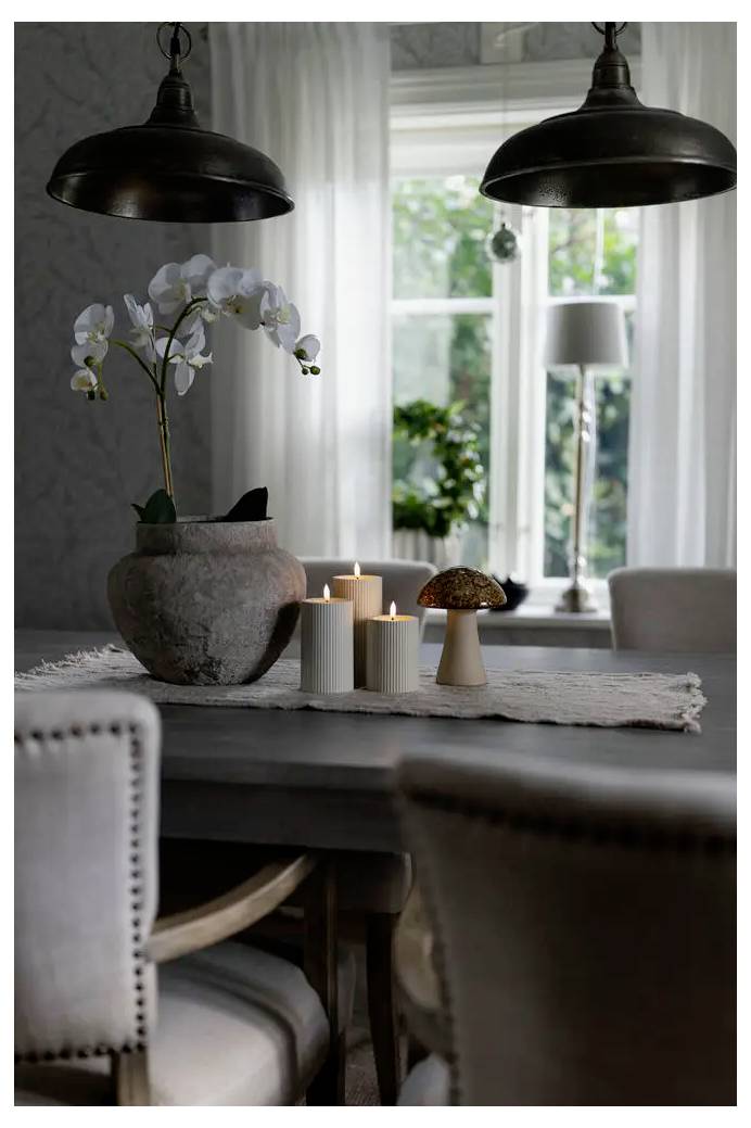 Eettafel met witte orchidee, kaarsen en een paddenstoel-vormige lamp in een zacht verlichte eetkamer nabij een helder raam.