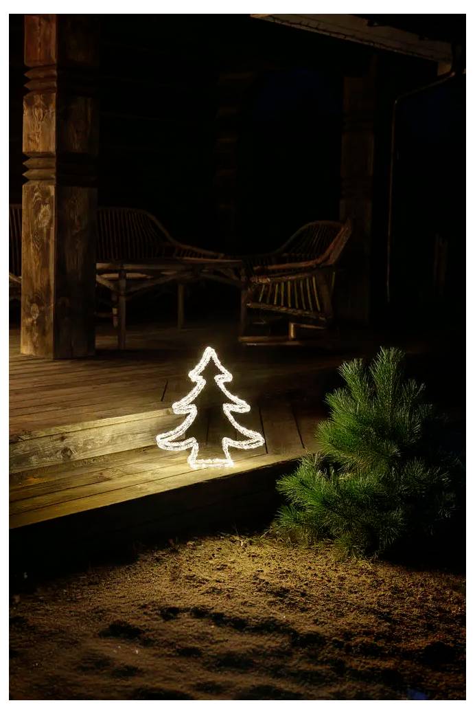 Verlichte kerststoomlijning op een veranda-trap naast een kleine altijdgroene struik 's nachts, met een donker houten huisje en stoelen op de achtergrond.