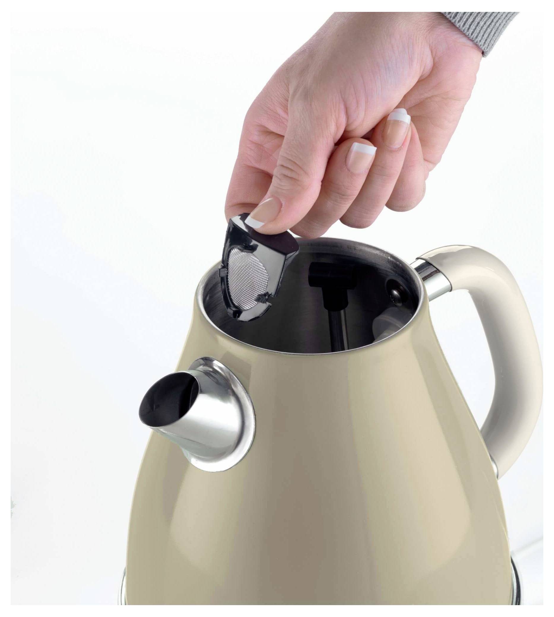 Hand laat een theezakje in een beige elektrische waterkoker vallen met het deksel open.