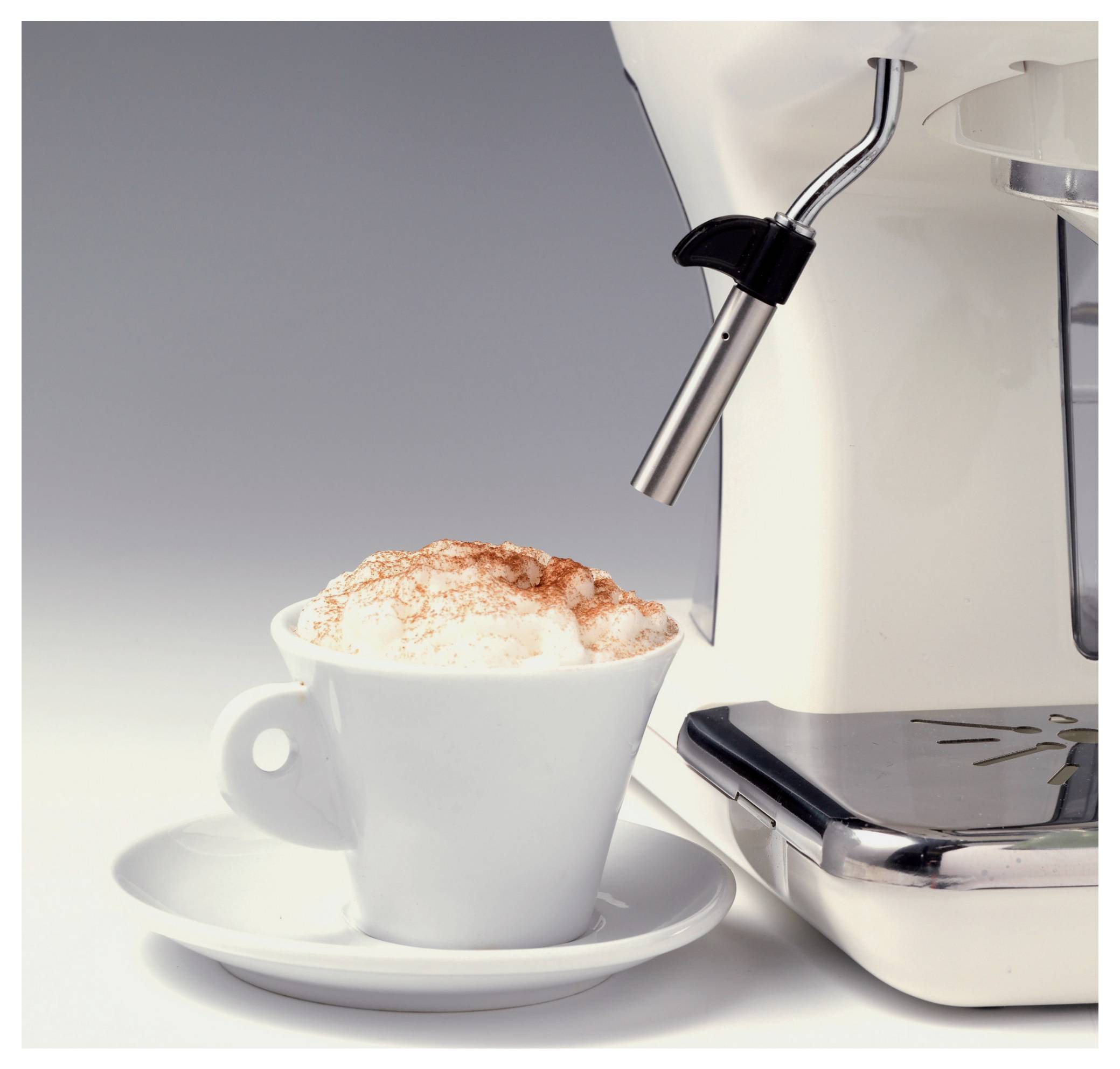 Witte kop met schuimige koffie op een schoteltje naast een roestvrijstalen espressomachine die schuim afgeeft.