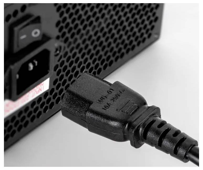 Close-up van een stroomstekker die in de achterkant van een elektronisch apparaat met een geventileerd paneel is gestoken.
