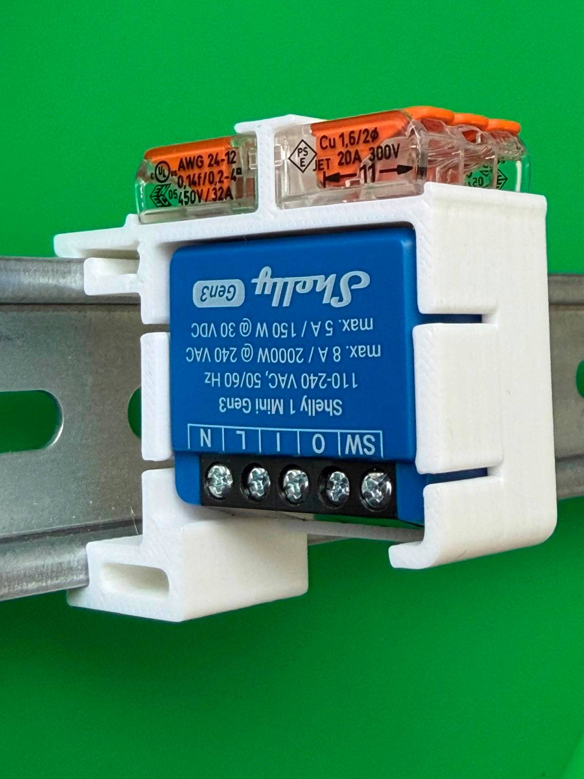 DIN-rail gemonteerde Shelly slimme relaismodule met klemschroeven en duidelijk bedradingsdeksel op een groene achtergrond.