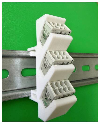 Drie 3D-geprinte veerclips houden opgevouwen geld op een metalen rail tegen een helder groene achtergrond vast.