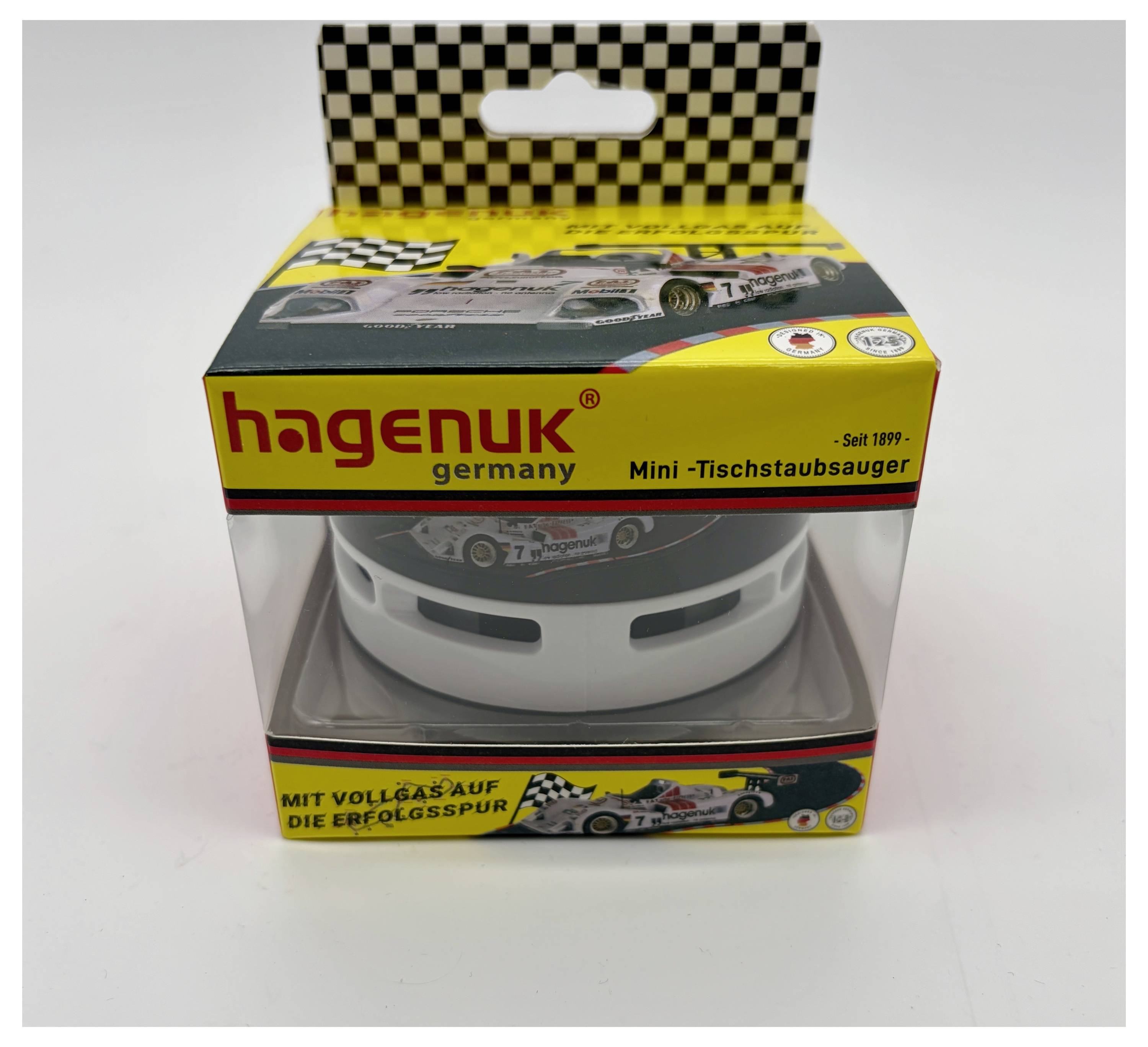 Verpakte HAGENUK mini bureaubladstofzuiger met racewagen-thema verpakking en een duidelijk venster dat het witte apparaat binnenin toont.