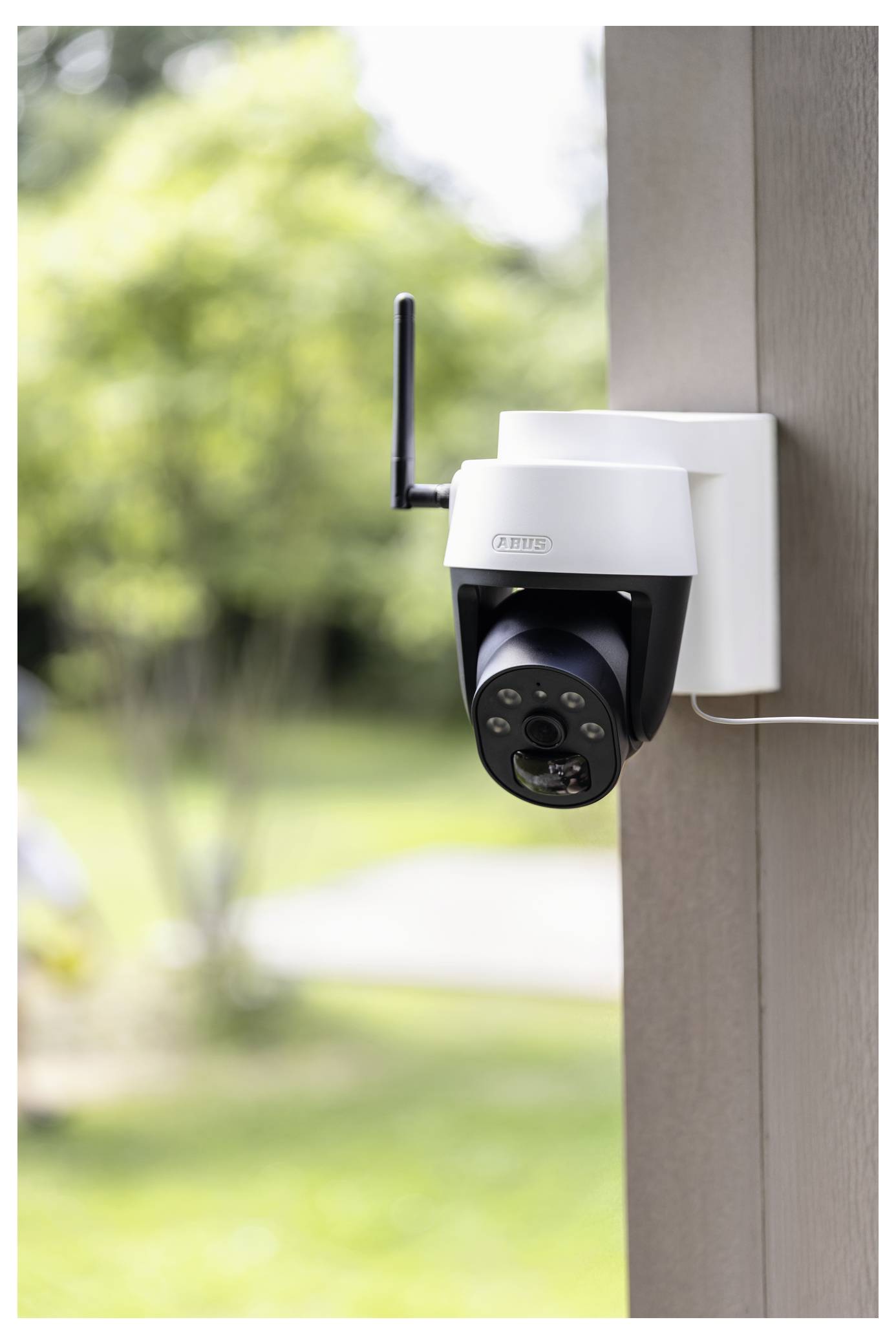 Buitenbeveiligingscamera met antenne gemonteerd op een paal, uitkijkend over een onscherpe tuin en looppad.