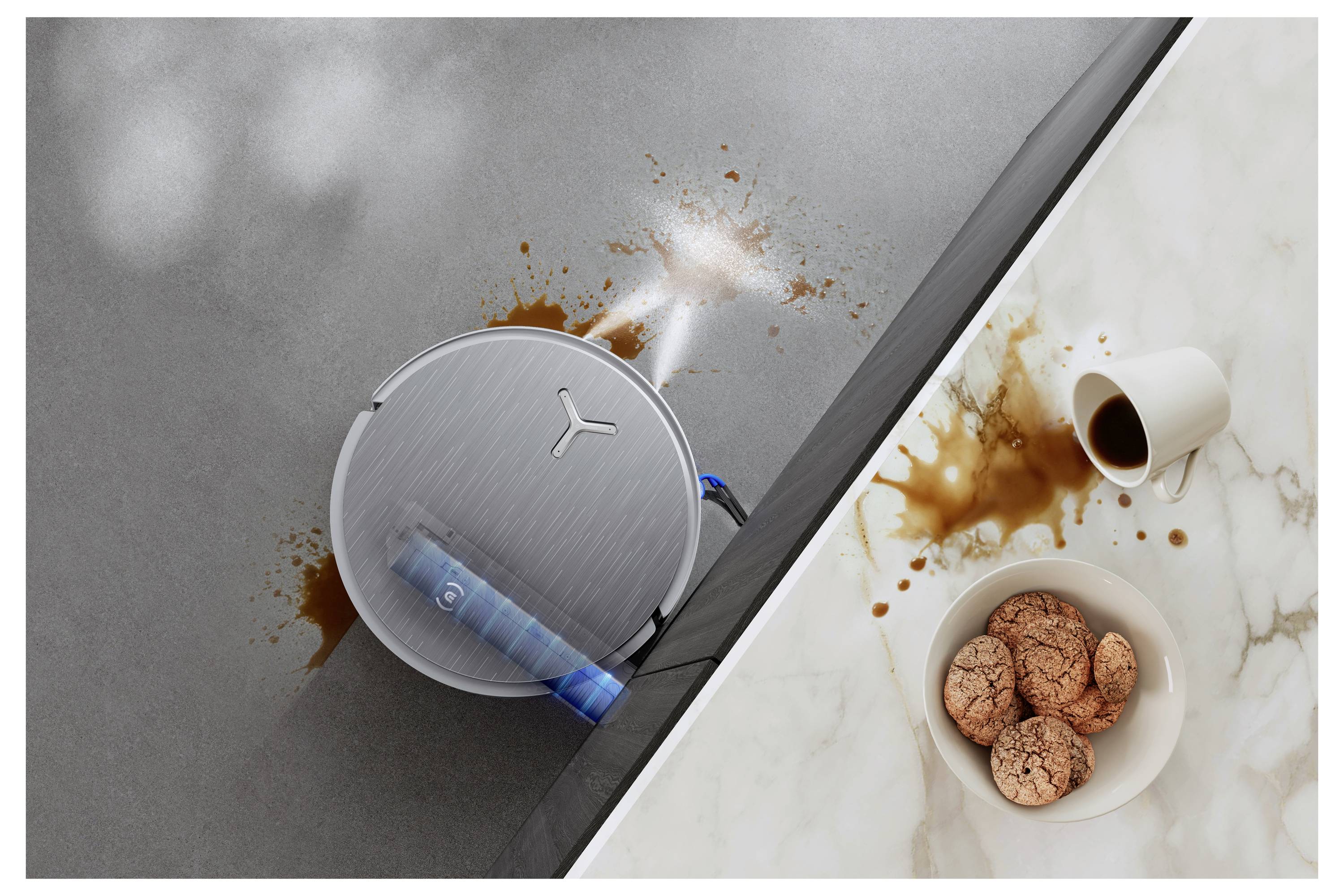 Gemorste koffie op een aanrecht naast een robotstofzuiger die aan het schoonmaken is, in de buurt van een kom koekjes en een omgevallen koffiekopje.