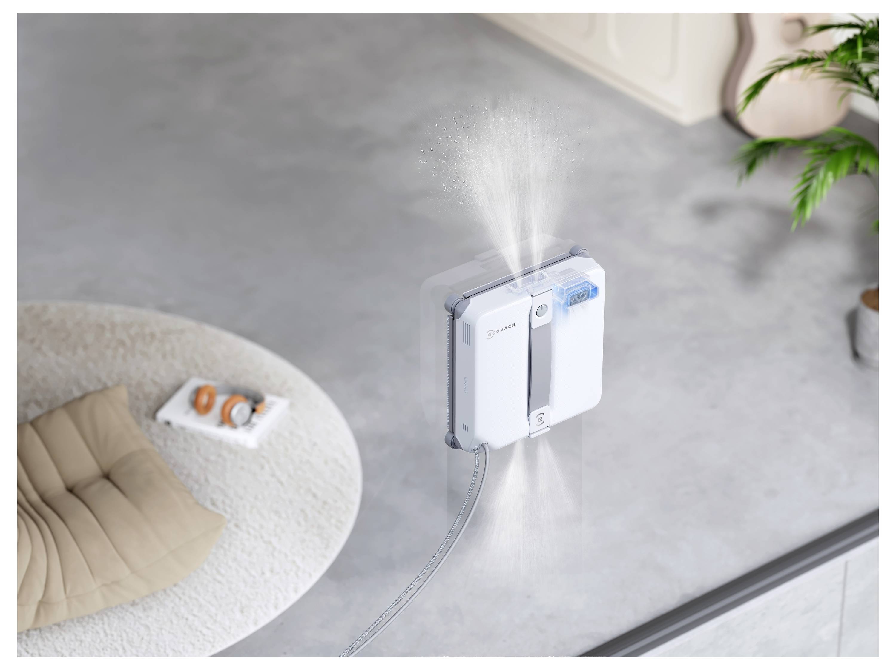 Een raamschoonmaakrobot is aan een glazen paneel bevestigd en spuit mist uit terwijl deze schoonmaakt, gezien van bovenaf in een modern interieur.
