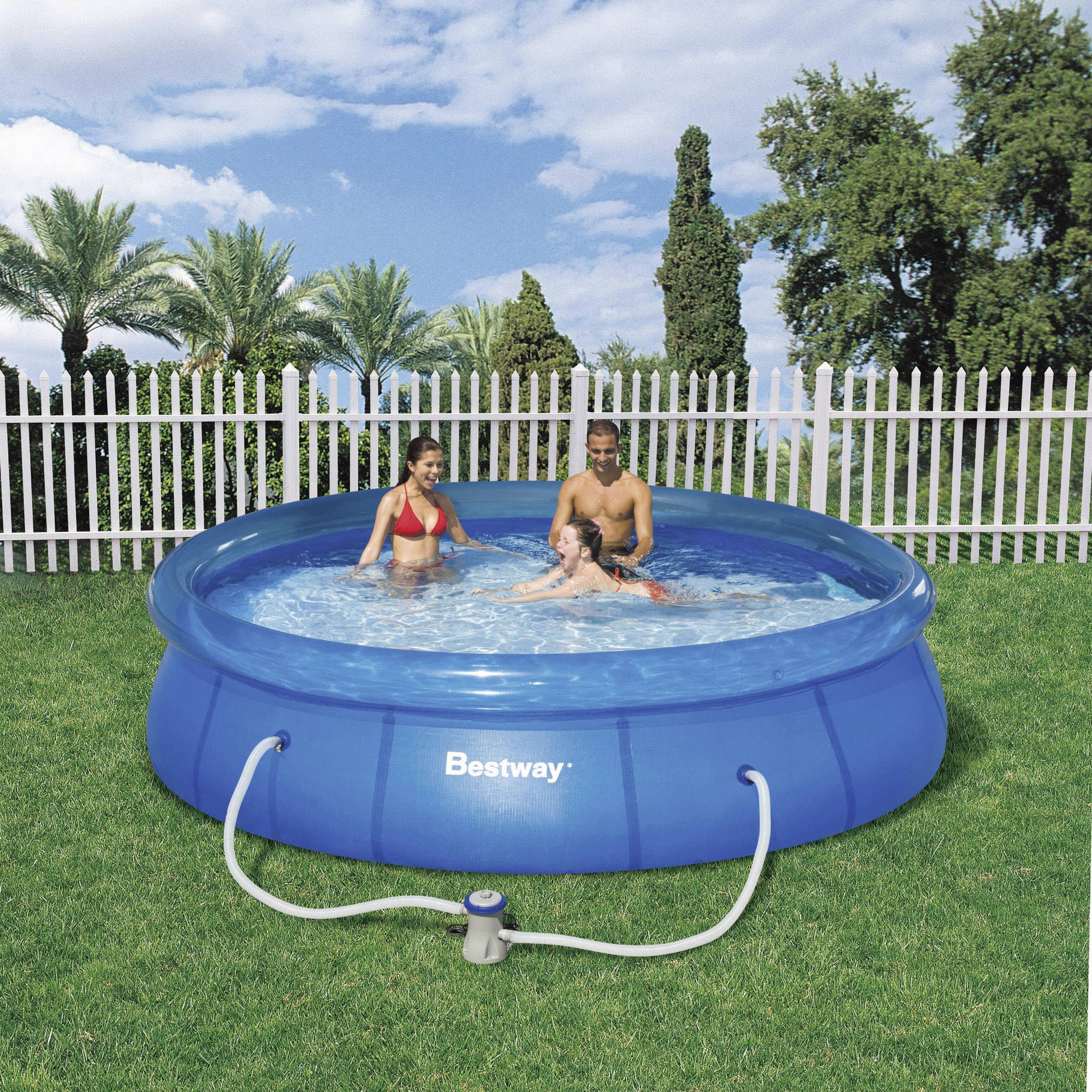 Drie personen spelen in een blauwe opblaasbare pool in een tuin. Een witte hek en bomen zijn op de achtergrond zichtbaar.