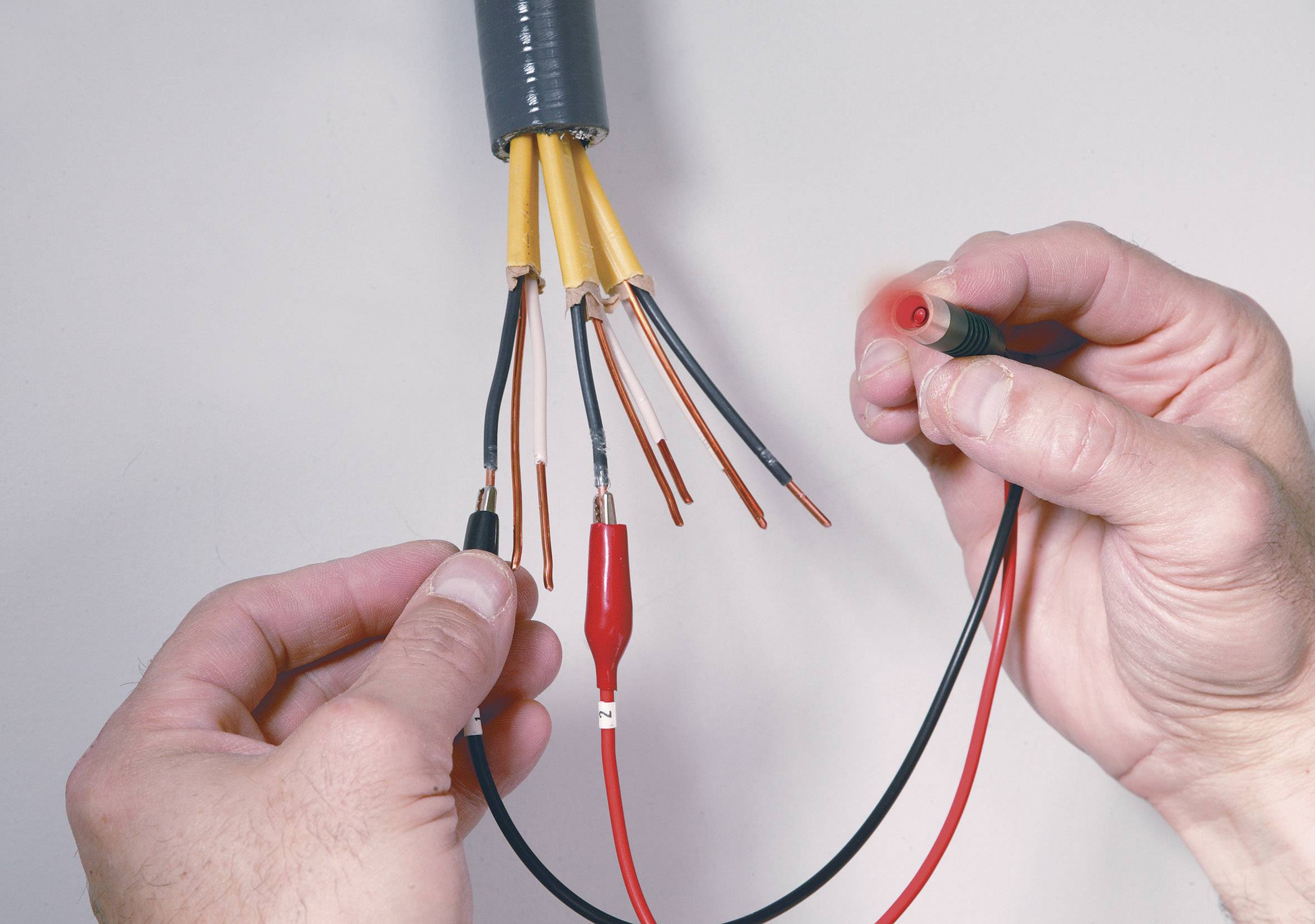 Een persoon meet met een multimeter de spanning van verschillende ontblote kabels om hun elektrische verbinding te controleren.