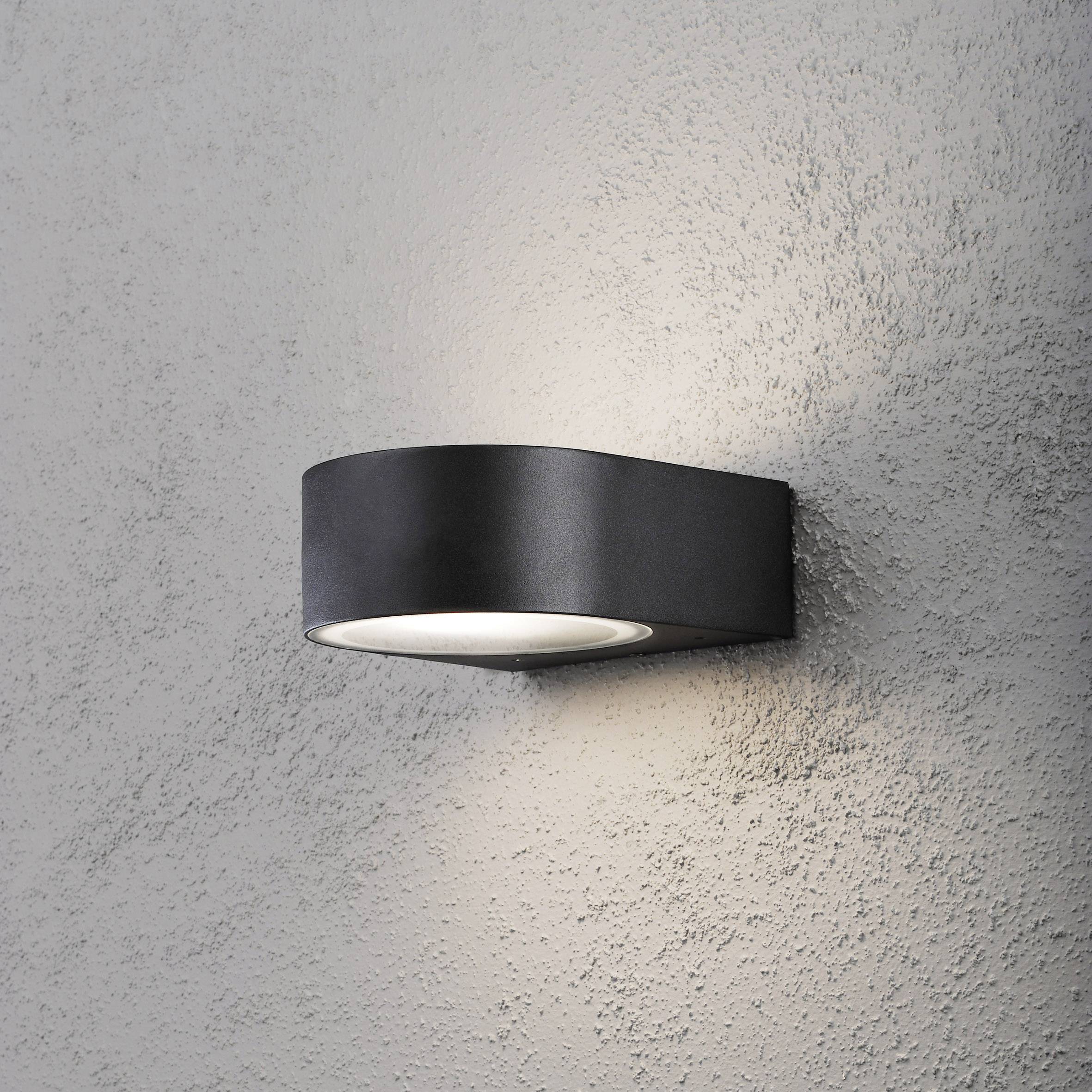 Wandlamp in modern design, die licht zacht tegen de muur projecteert. Donkere behuizing, geschikt voor hedendaagse interieurs.