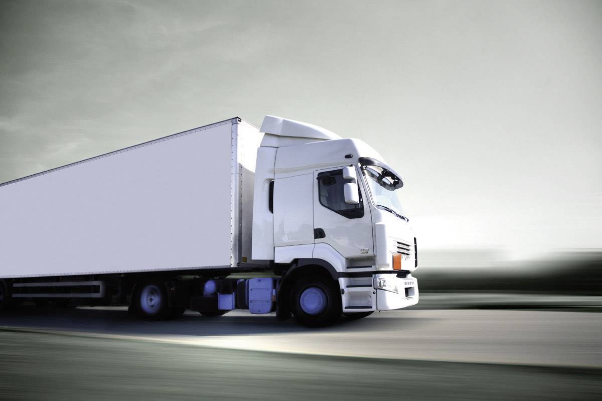 Een witte vrachtwagen rijdt op een snelweg met een onscherpe achtergrond. De lucht is bewolkt en geeft een dynamische beweging weer.