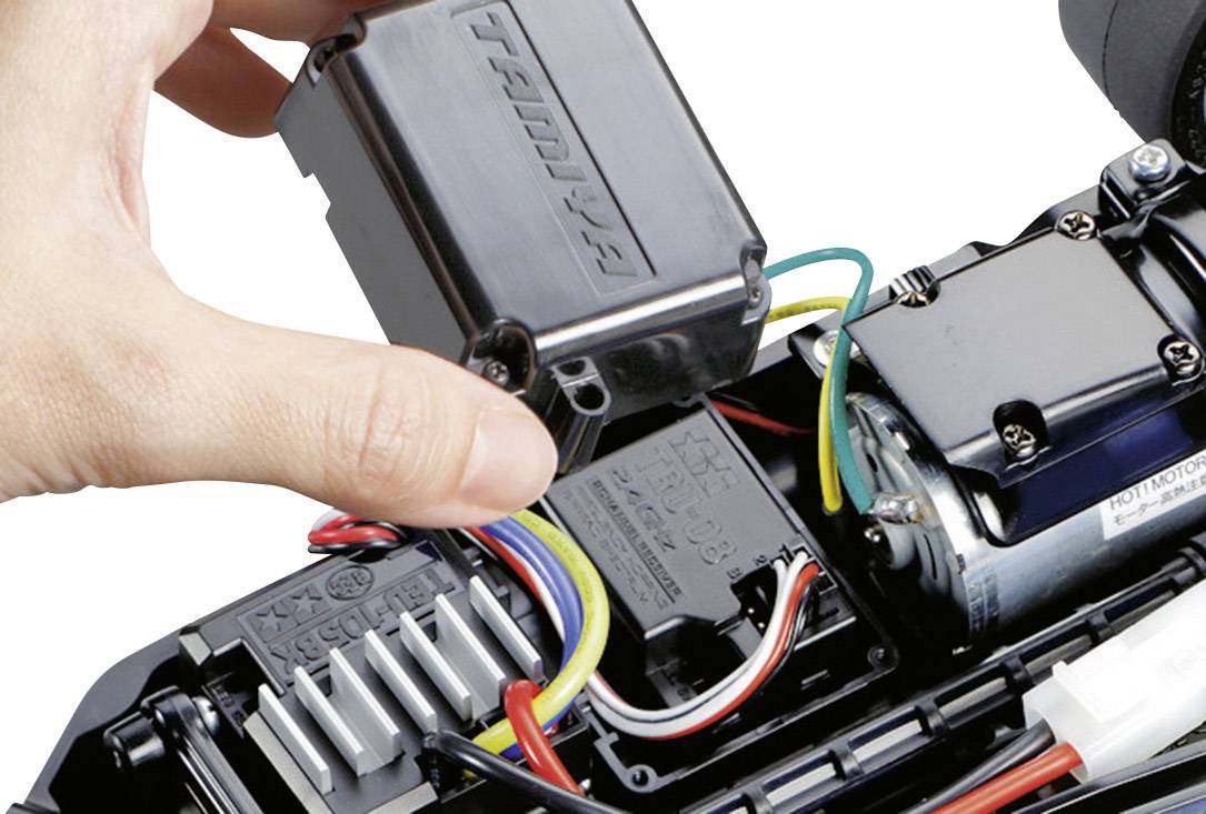 Een hand monteert een zwarte afdekking over een elektronische aansluiting in een mechanisch apparaat met gekleurde kabels.