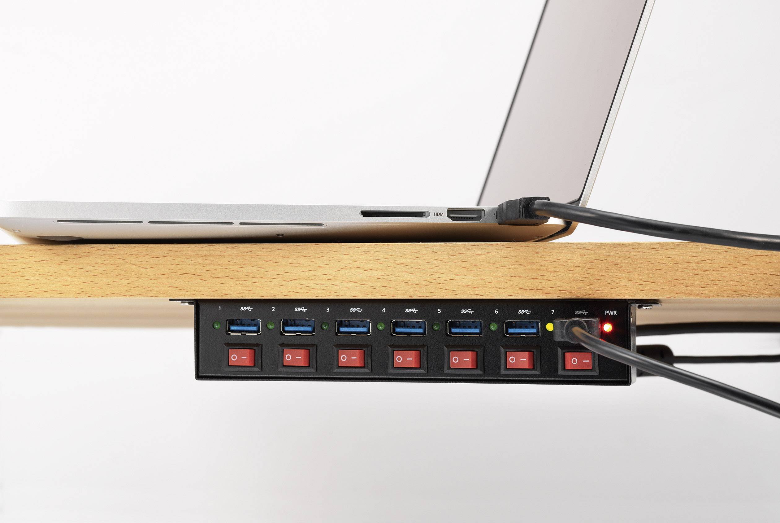 Een laptop is aangesloten op een USB-hub met meerdere poorten en schakelaars, die onder een houten tafel is gemonteerd.