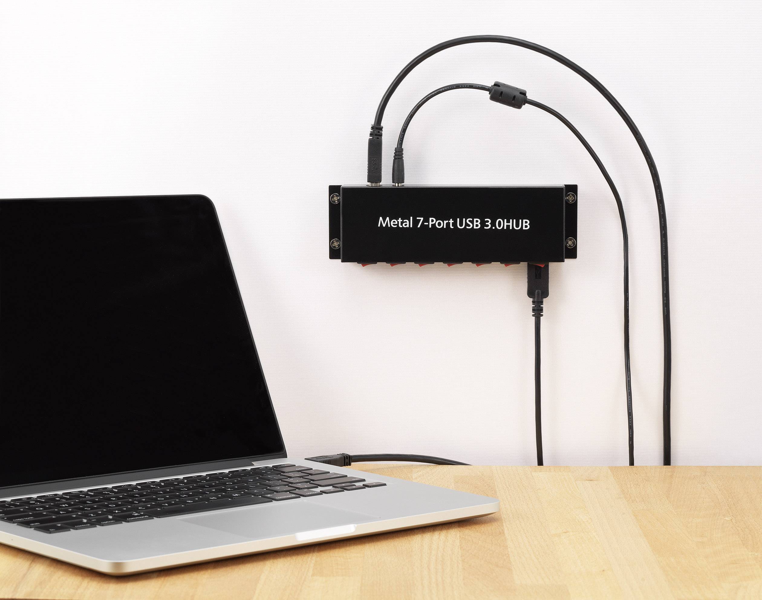 Laptop op houten tafel verbonden met een zwarte metalen USB-hub met zeven poorten. Twee USB-kabels zijn aangesloten.