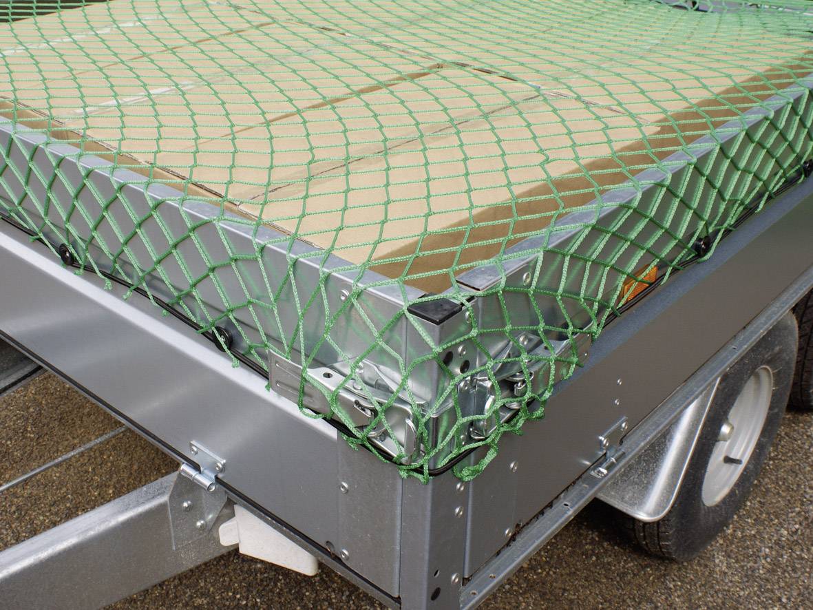 Aanhanger met groene netbedekking die platte dozen vastzet. Banden en metalen structuur van de aanhanger zichtbaar.